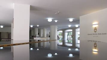 Eine moderne Hotelhalle mit spiegelndem Boden, großen Säulen und einer Rezeption.