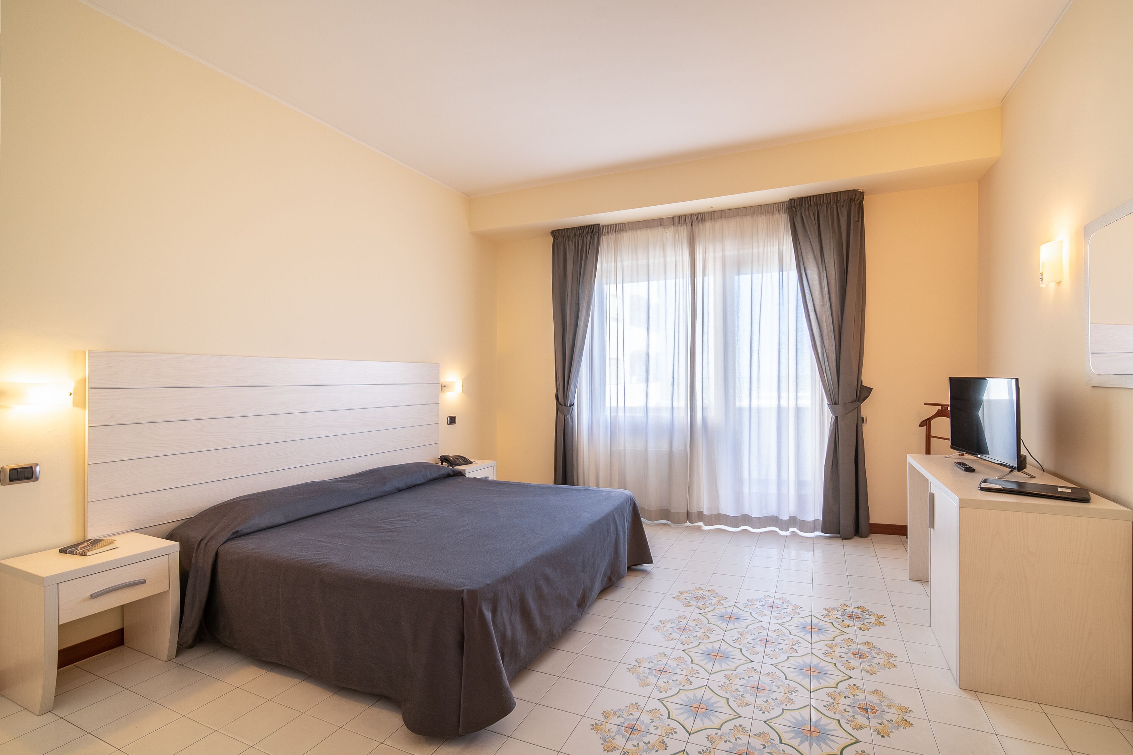 A hotel room with a bed, bedside table, TV, and a desk with a chair.
