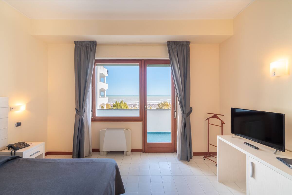 Habitación de hotel con cama, televisión, escritorio, silla, calefacción y vista al mar.