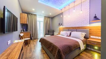A modern bedroom with a large bed, a desk, a chair, a TV, and a ceiling light.