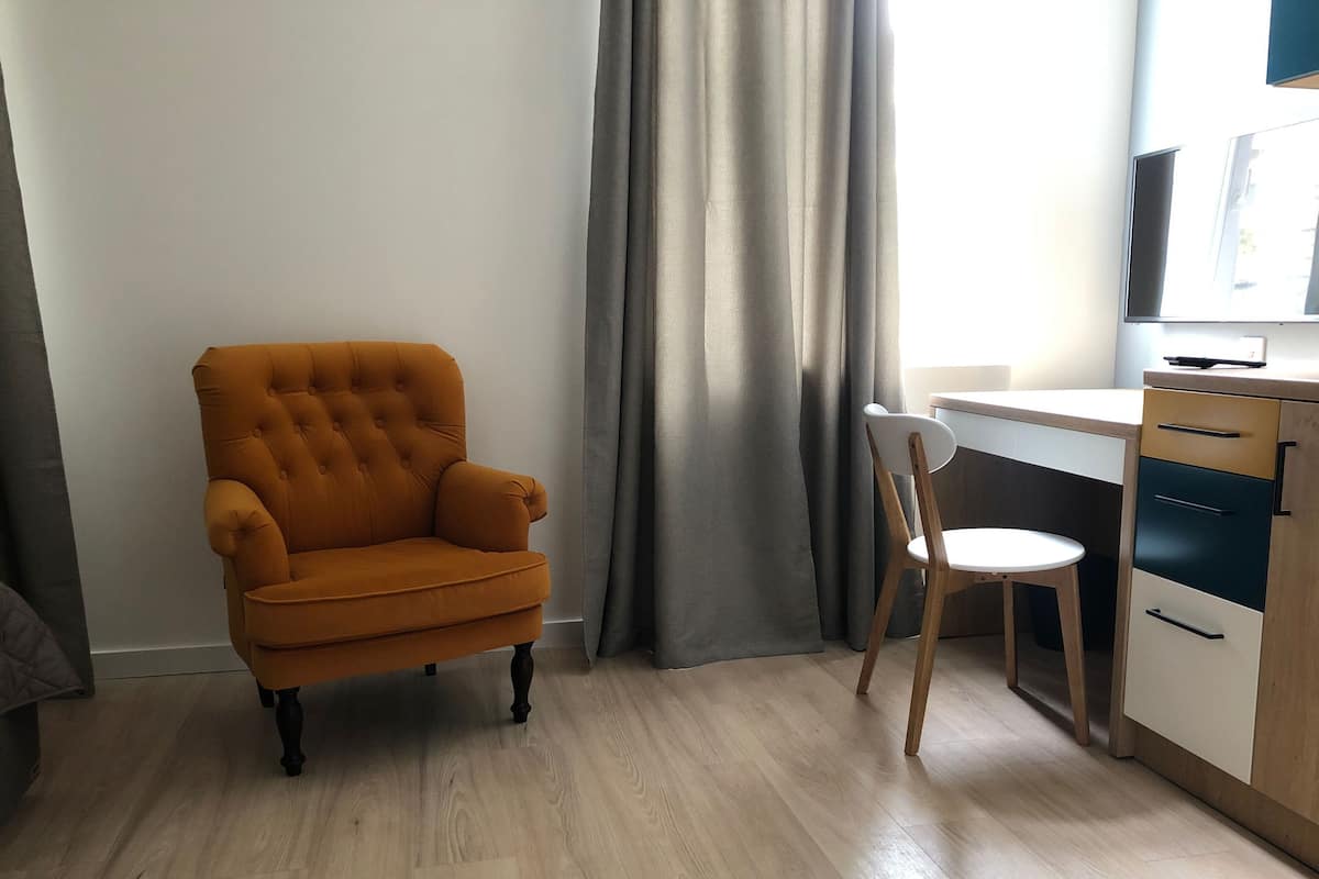 A room with a tufted armchair, a desk with a chair, and a cabinet with drawers.