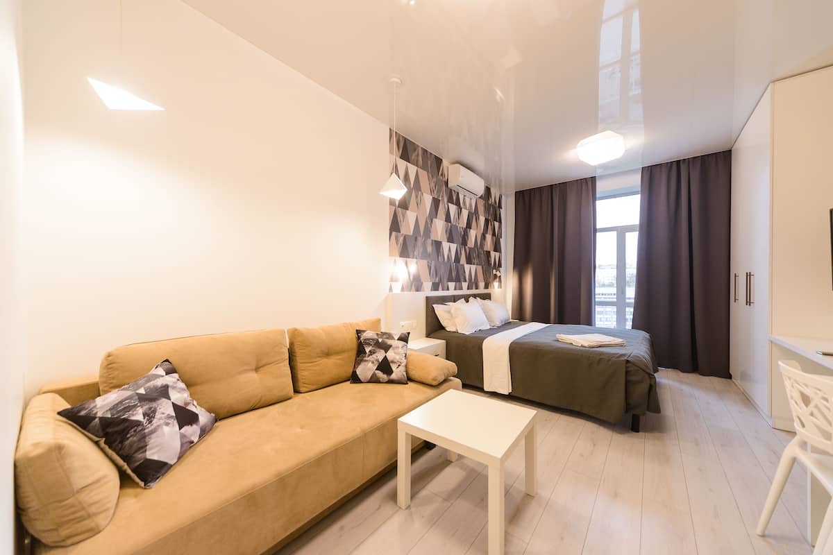 A modern hotel room with a sofa, a bed, a small table, and a desk.