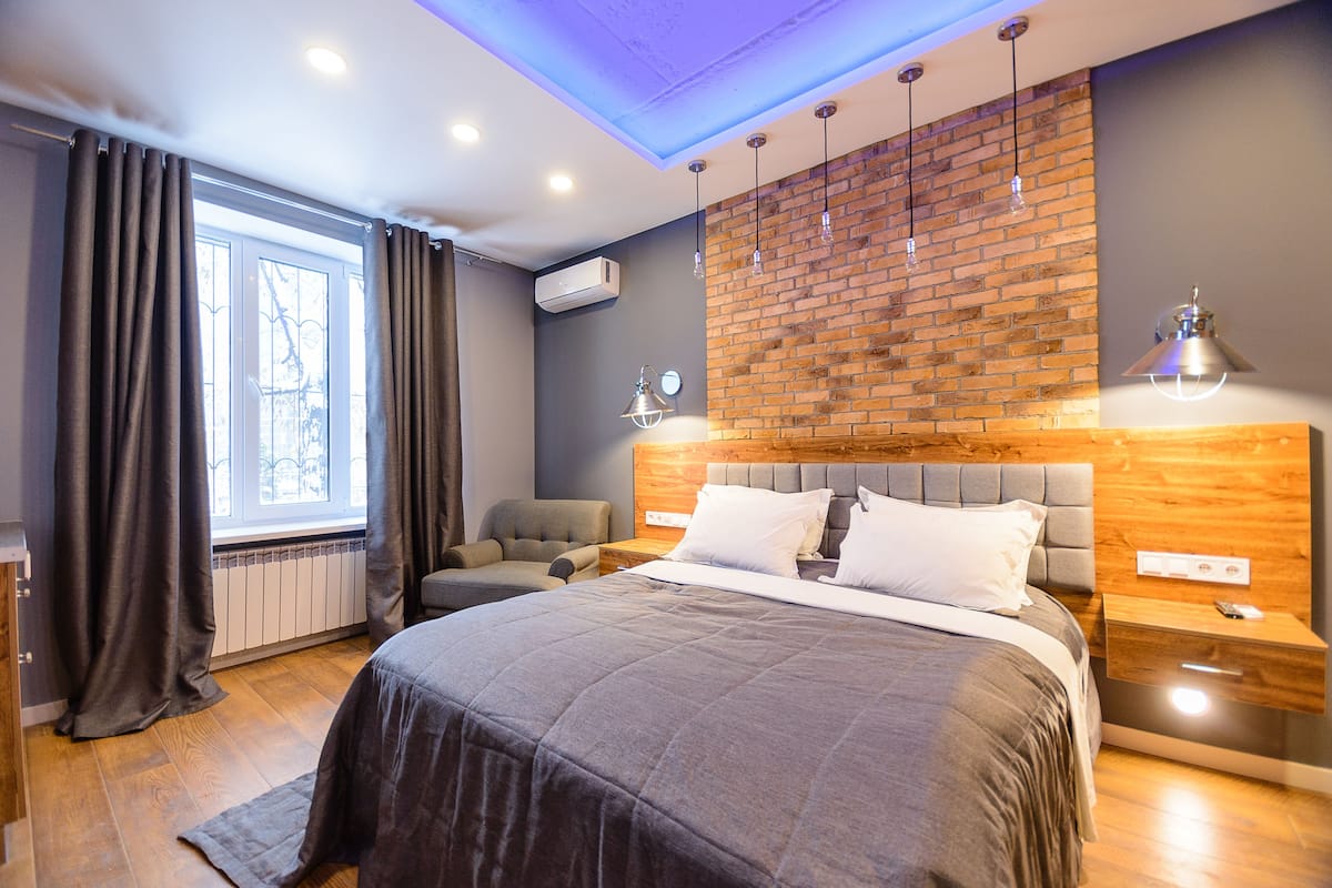 A modern bedroom with a large bed, a wooden headboard, a brick accent wall, and a window with curtains.