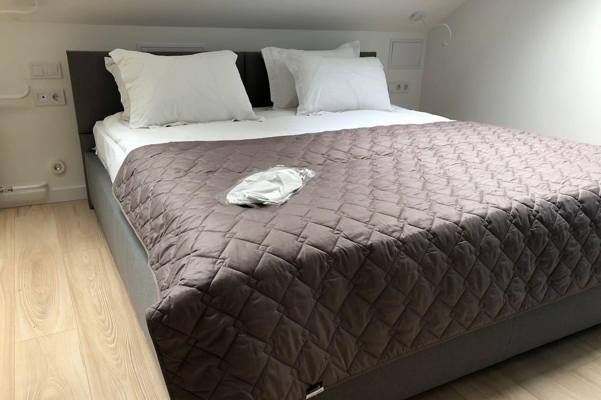 A neatly made bed with a brown quilt, white pillows, and a plastic bag on the bed.