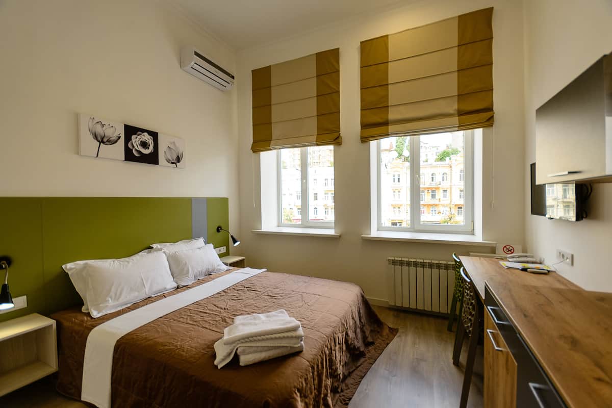A hotel room with a bed, a desk, and a view of buildings outside the window.