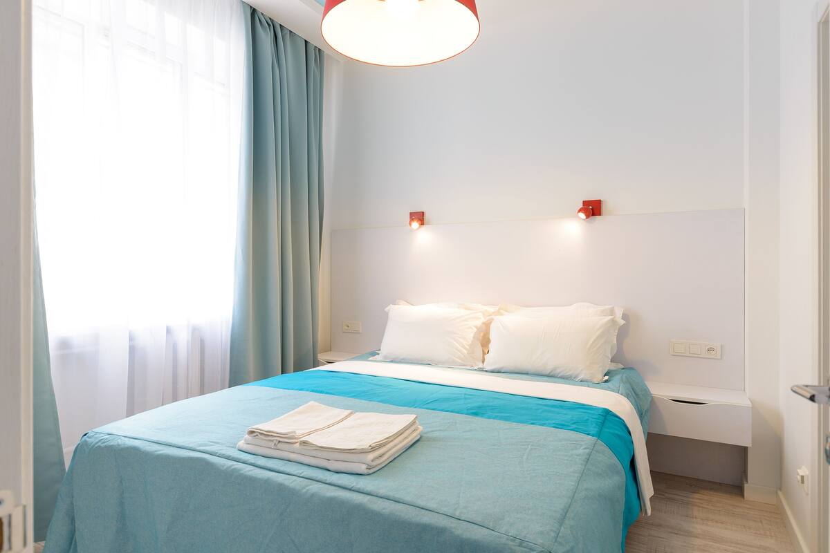 A hotel room with a bed, a nightstand, a lamp, and a window with curtains.