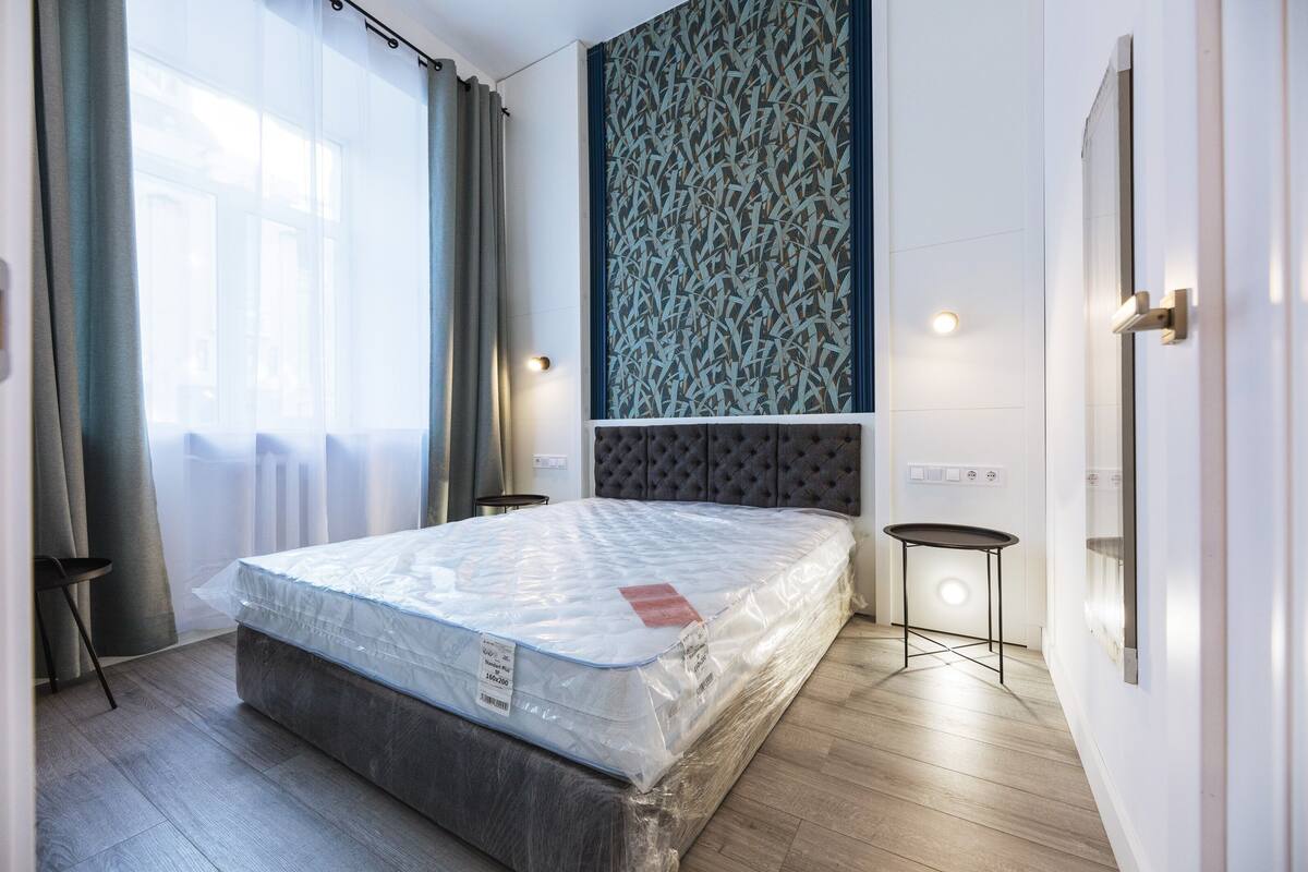 A modern bedroom with a large bed, a headboard, a small table, and a patterned wall.