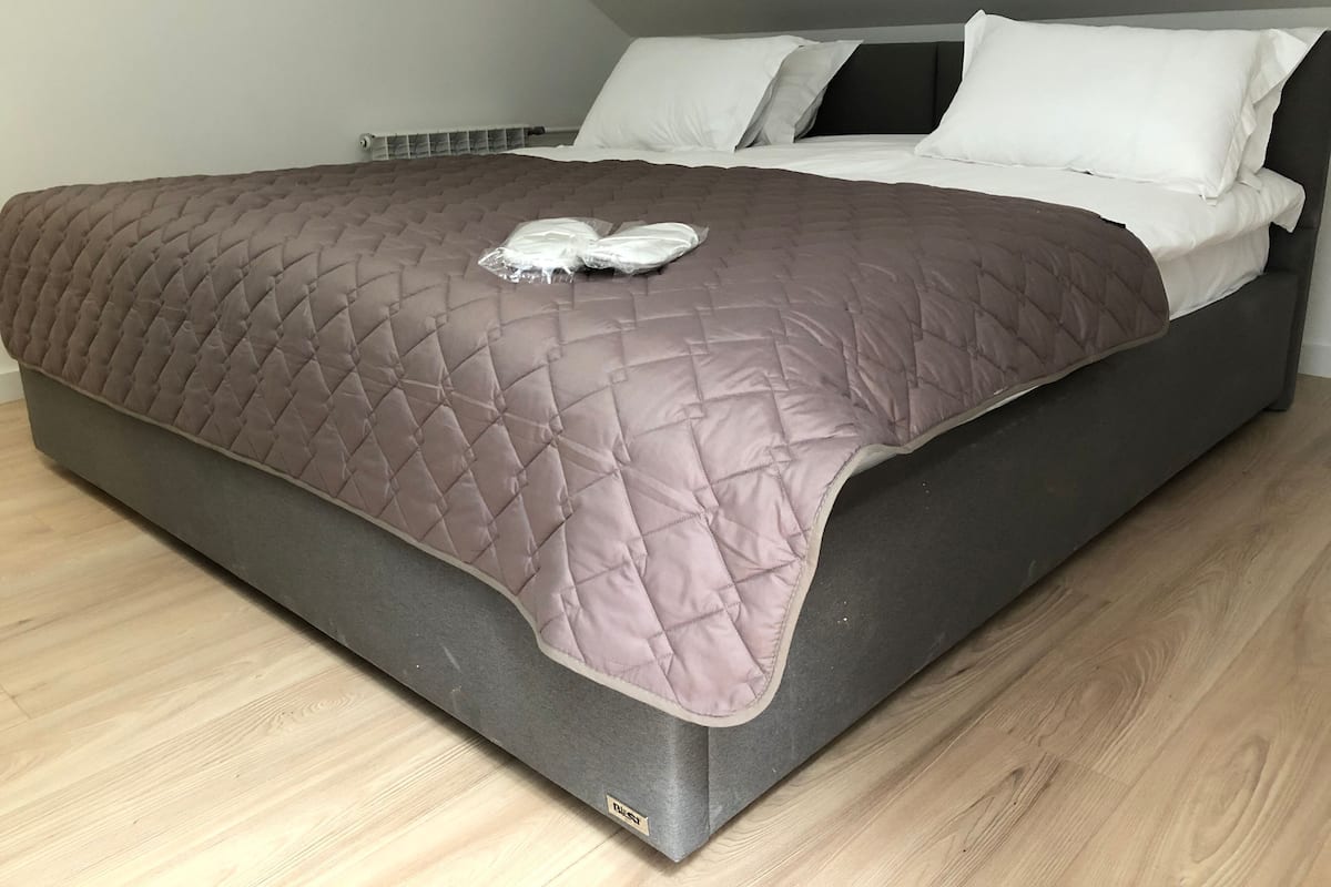 A modern bed with a quilted brown cover, white pillows, and a grey headboard in a room with wooden flooring.