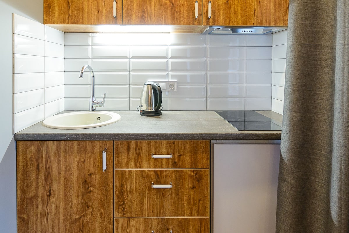 A compact kitchen with wooden cabinets, a sink, and a kettle.