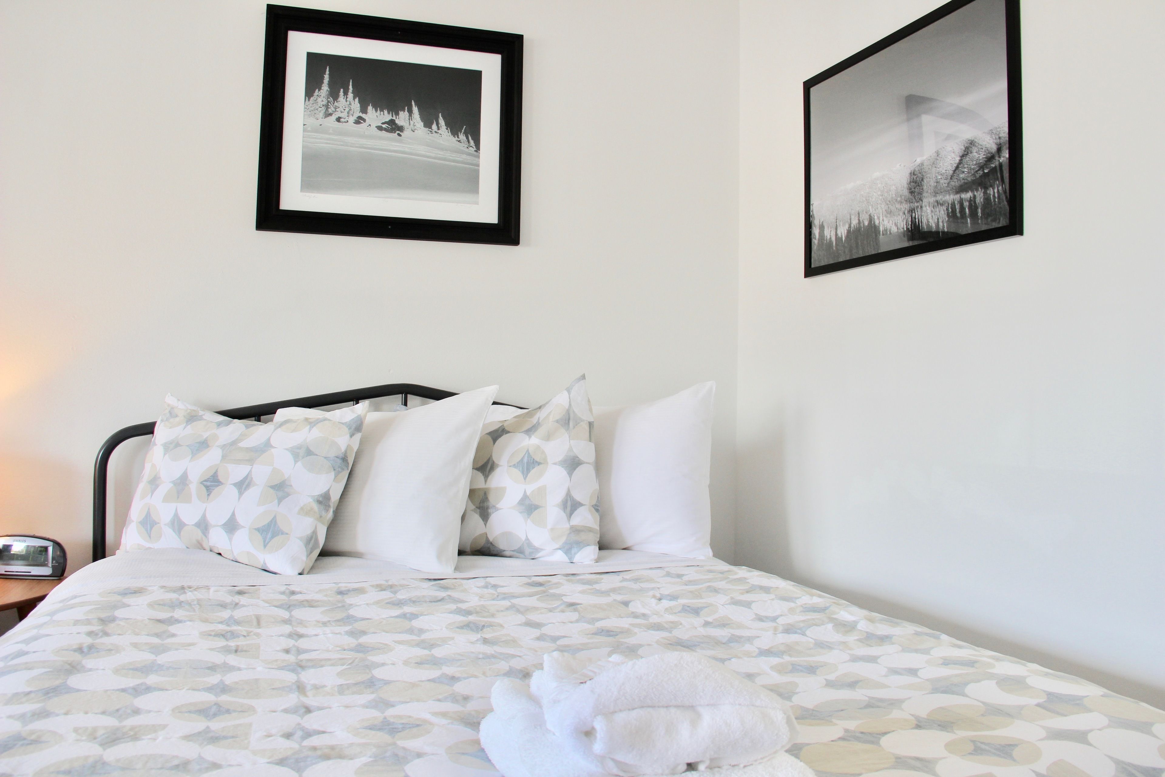 A neatly made bed with patterned bedding, a white towel, and two framed pictures on the wall.