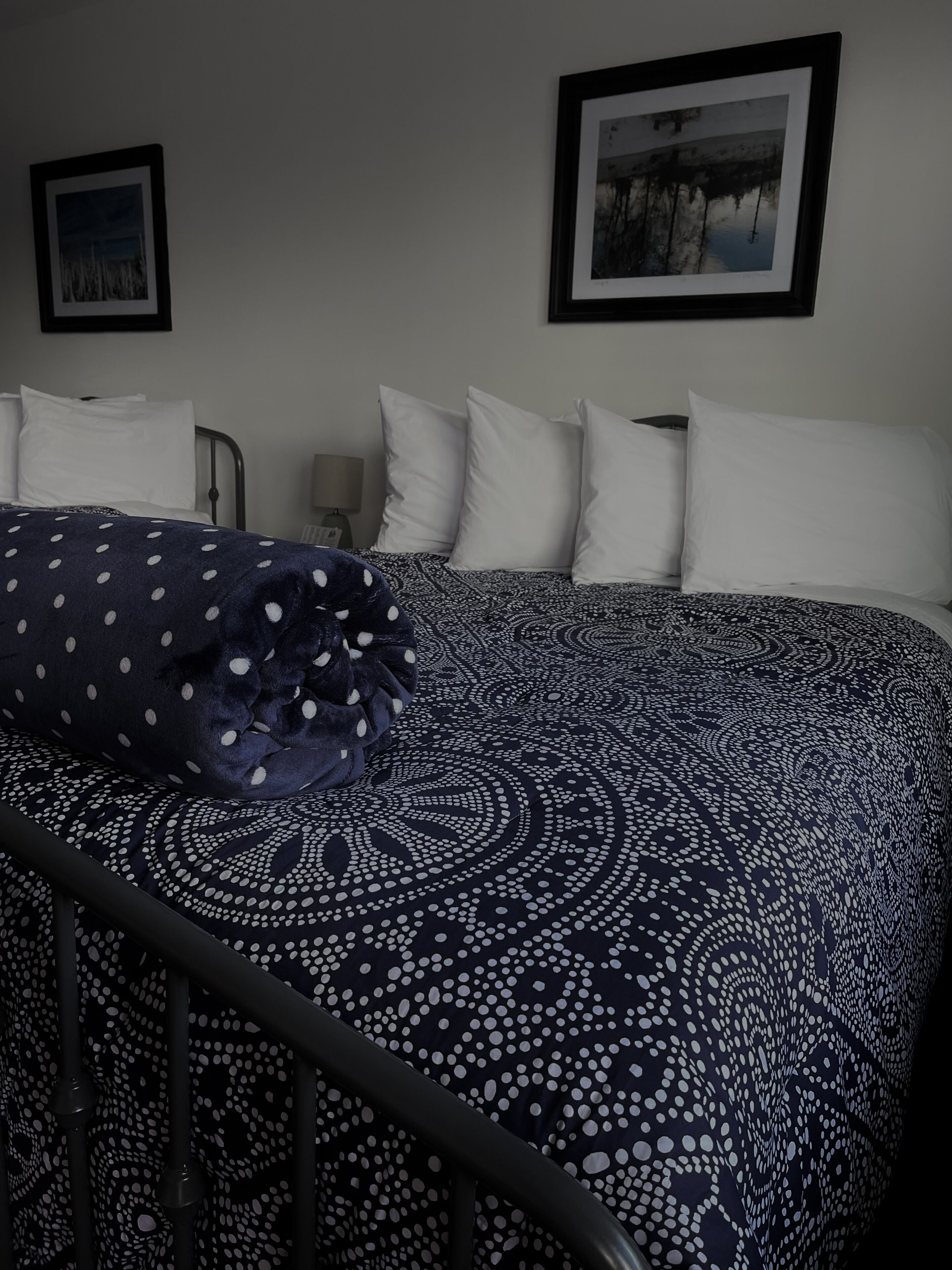 A bedroom with a bed, white pillows, a polka-dotted blanket, and two framed pictures on the wall.