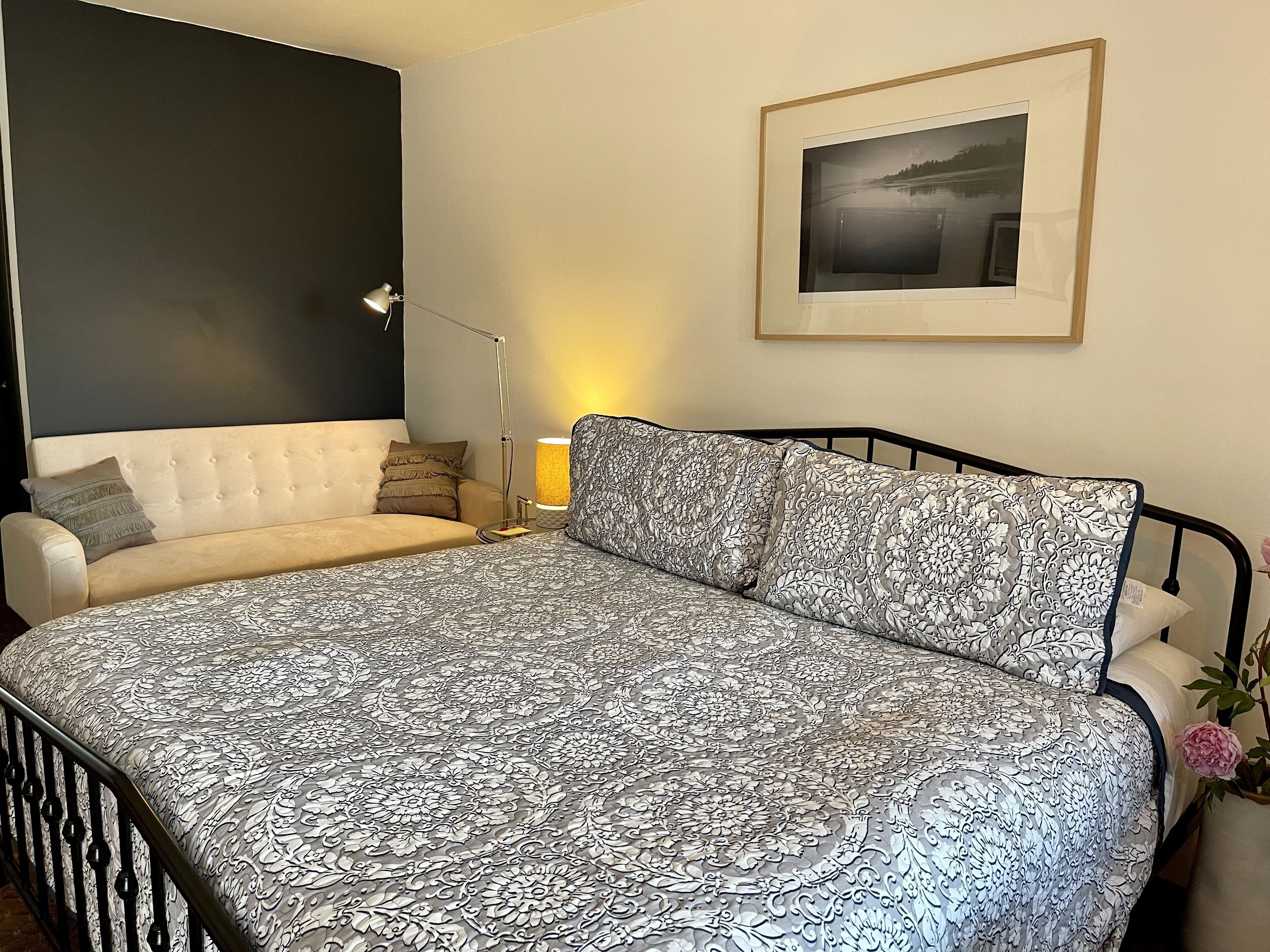 Une chambre à coucher avec un lit, un canapé, une lampe et un tableau encadré au mur.