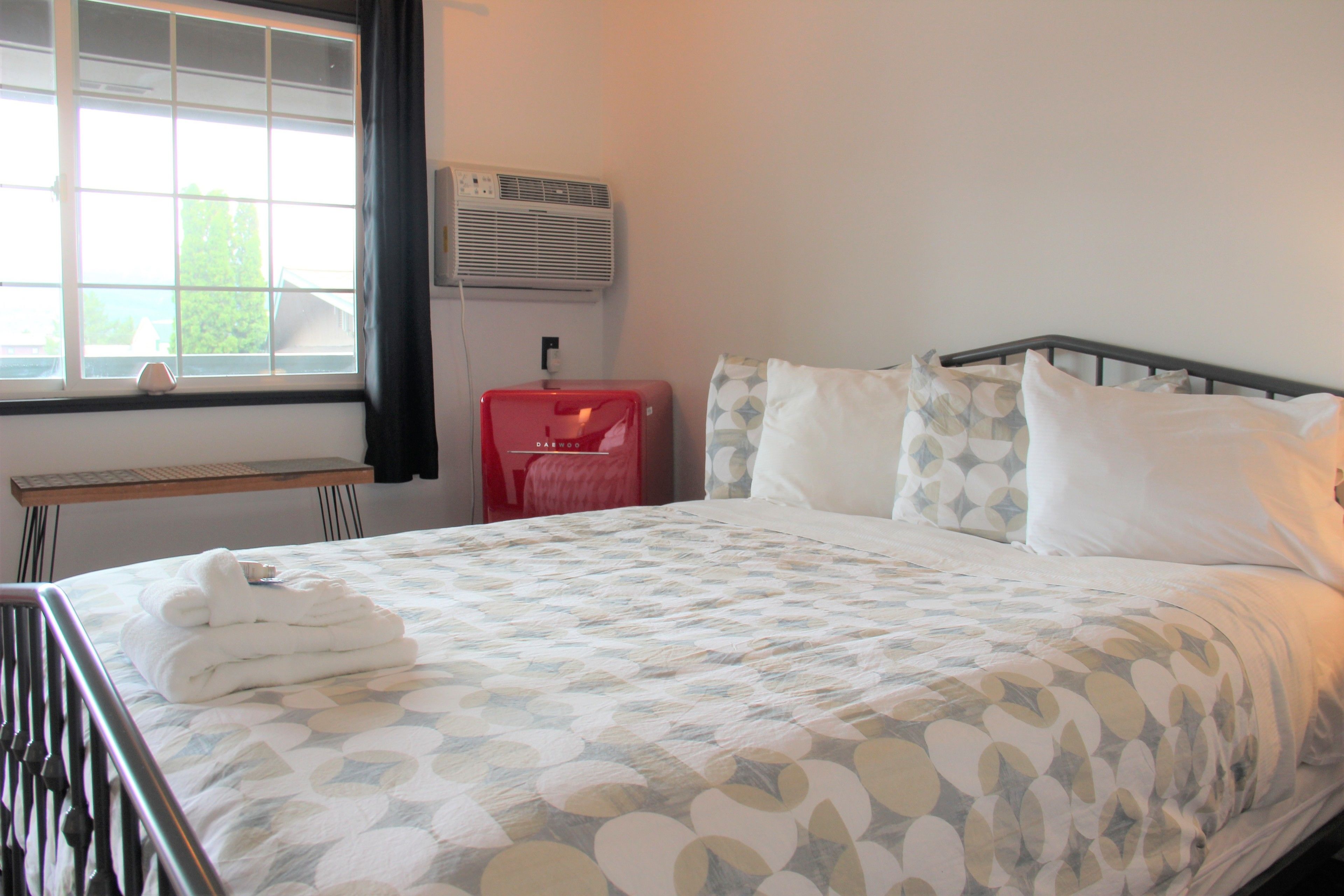 A neatly made bed with a patterned bedspread, a bedside table with a lamp, and a window with curtains.