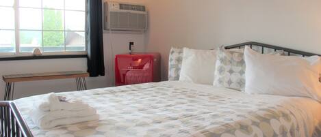 A neatly made bed with a patterned bedspread, a bedside table with a lamp, and a window with curtains.