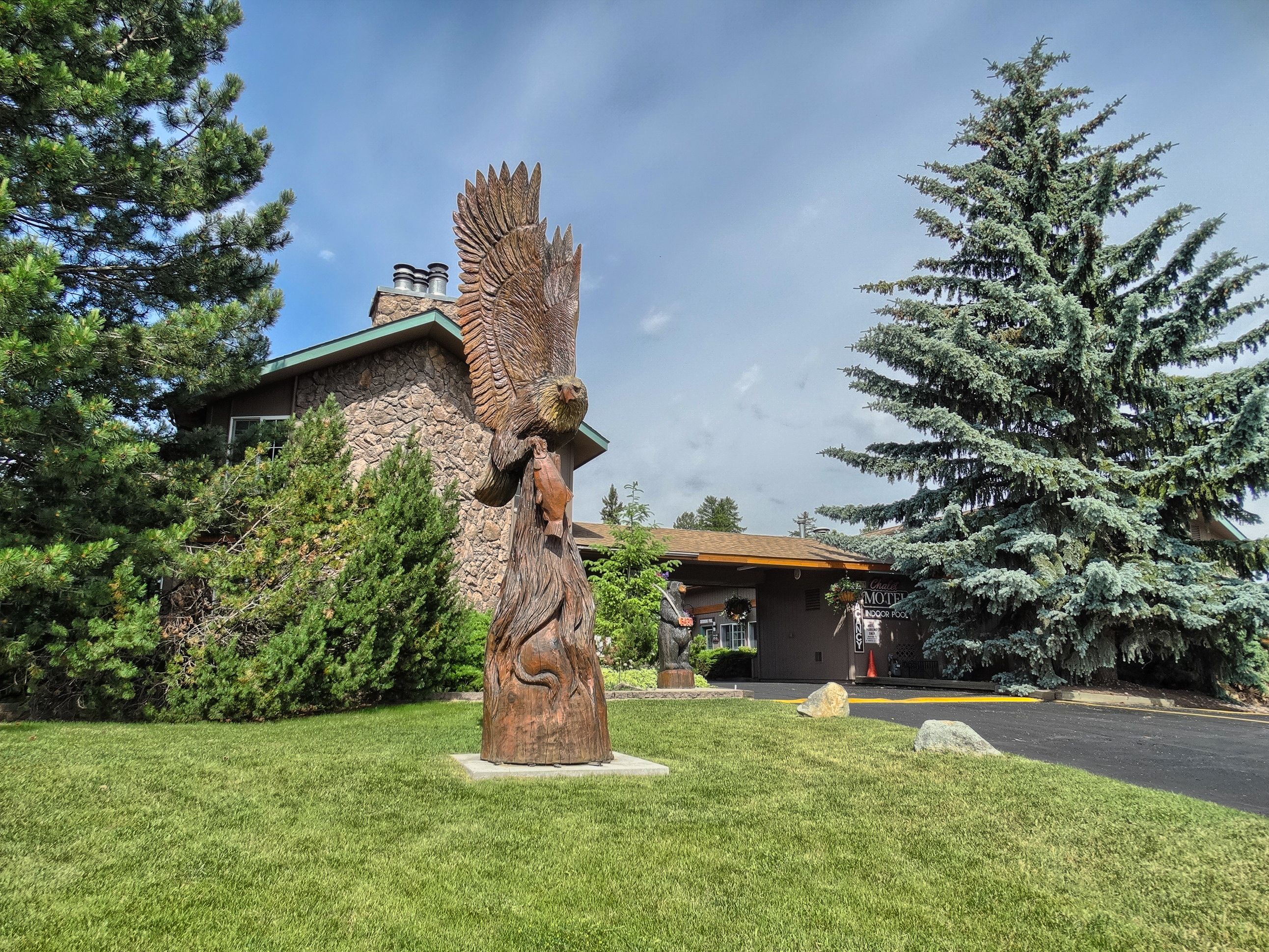 A rustic building with a stone facade and a large wooden sculpture of a tree with a bird.