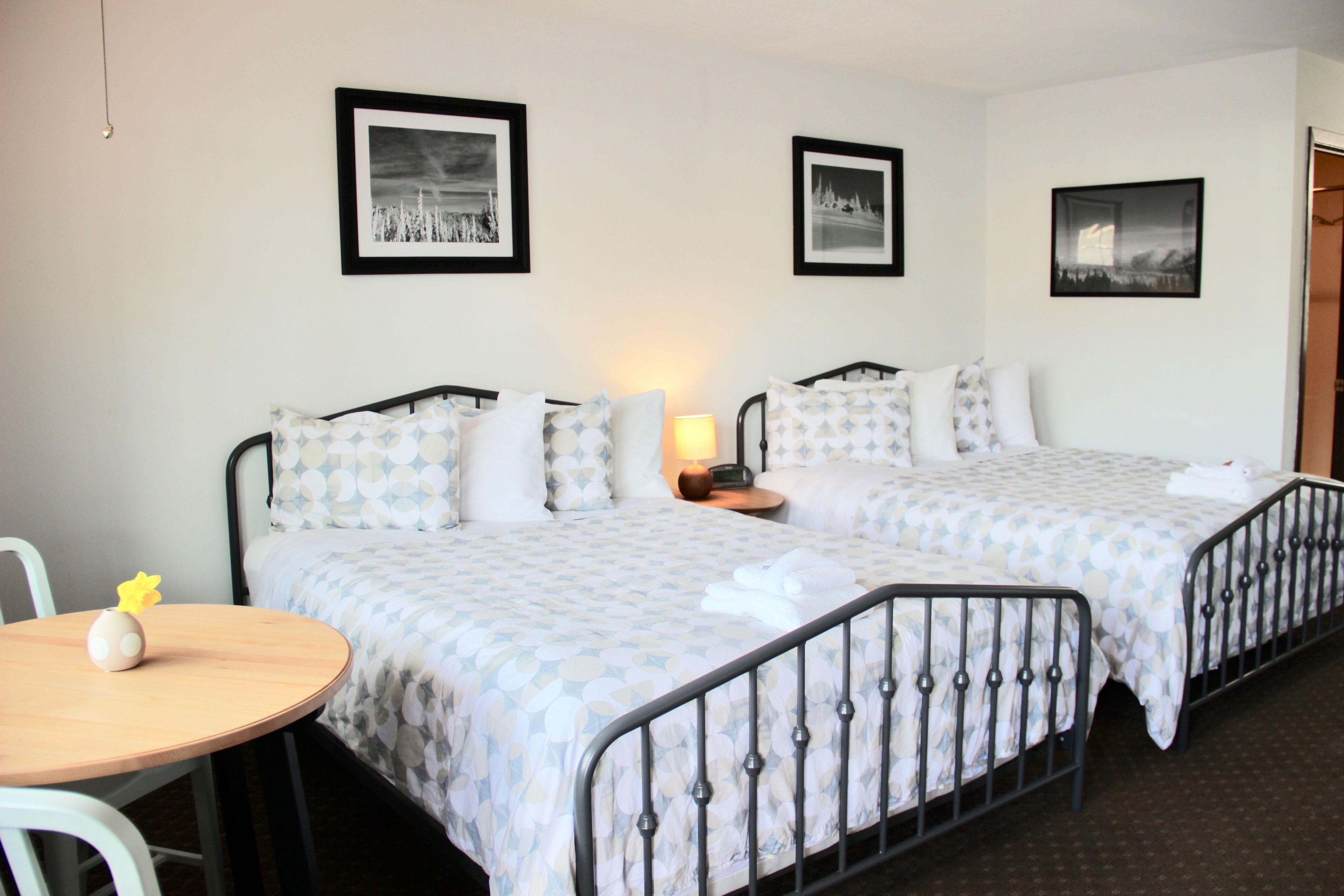 Habitación de hotel con dos camas, una mesita y una silla. Se observan cuadros enmarcados en la pared y una lámpara en la mesita de noche.