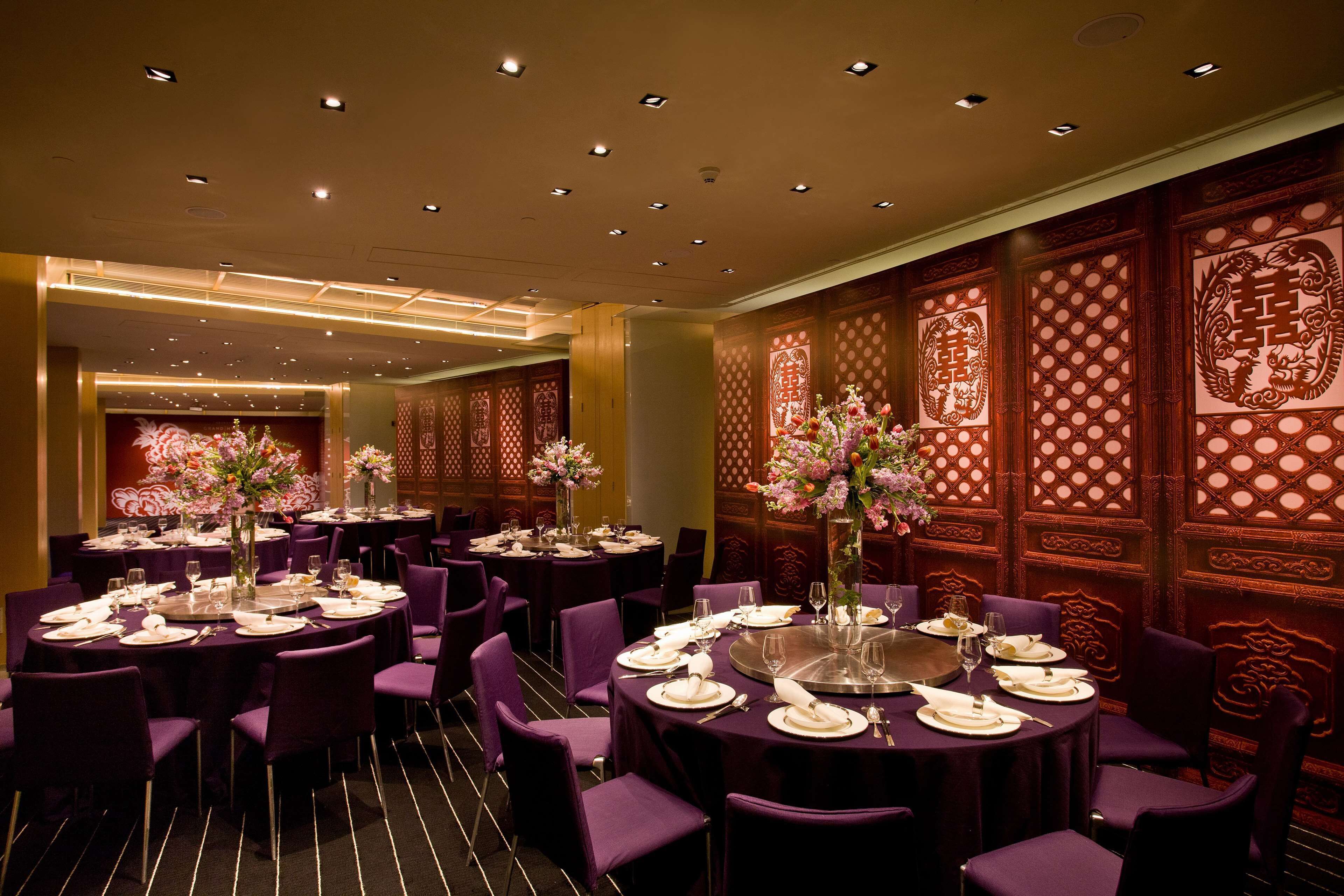A banquet hall with round tables set for dining, featuring purple chairs and floral centerpieces.