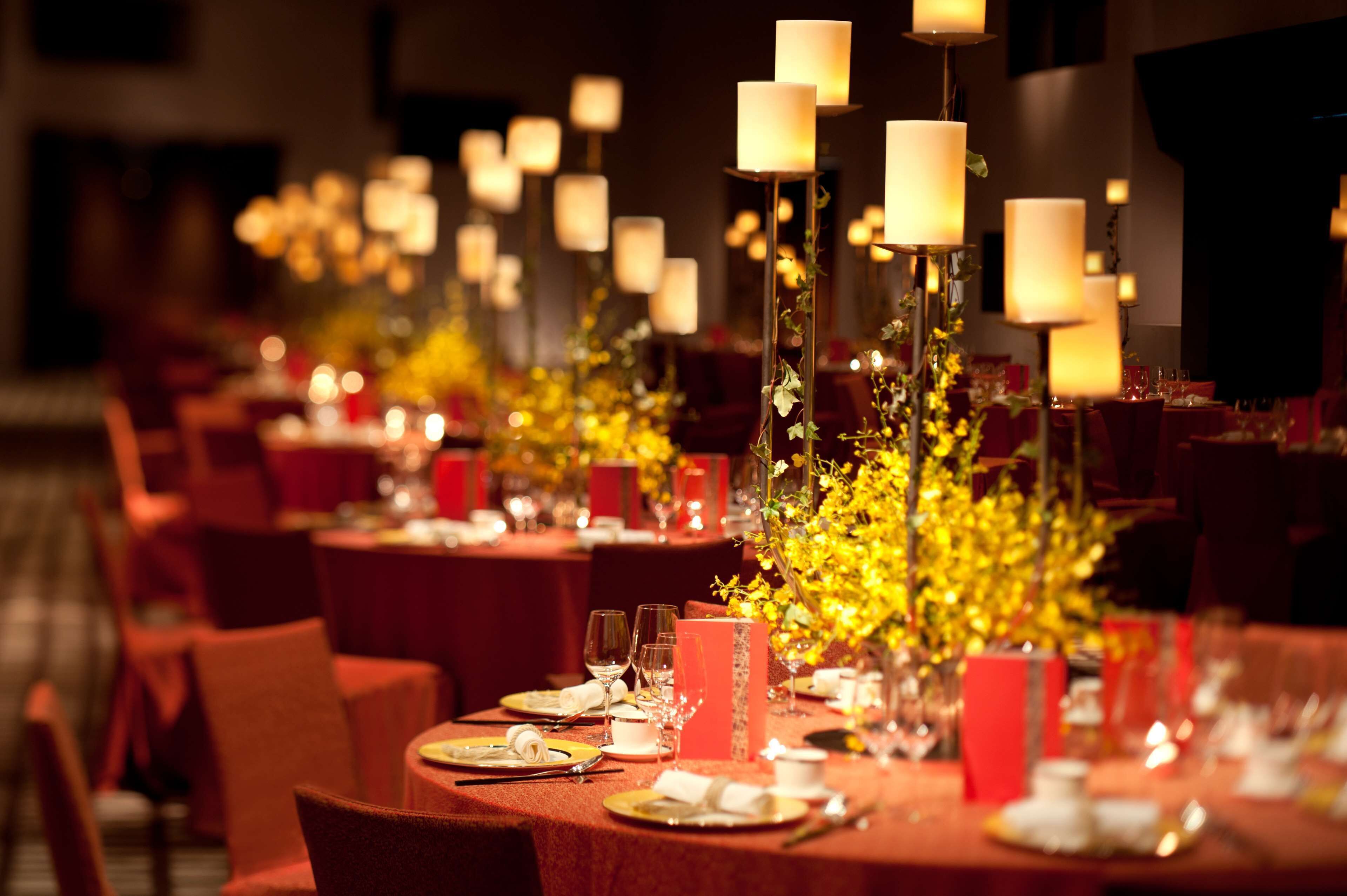 Un salón de banquetes con mesas dispuestas para un evento formal, con centros de mesa a la luz de las velas y manteles rojos.