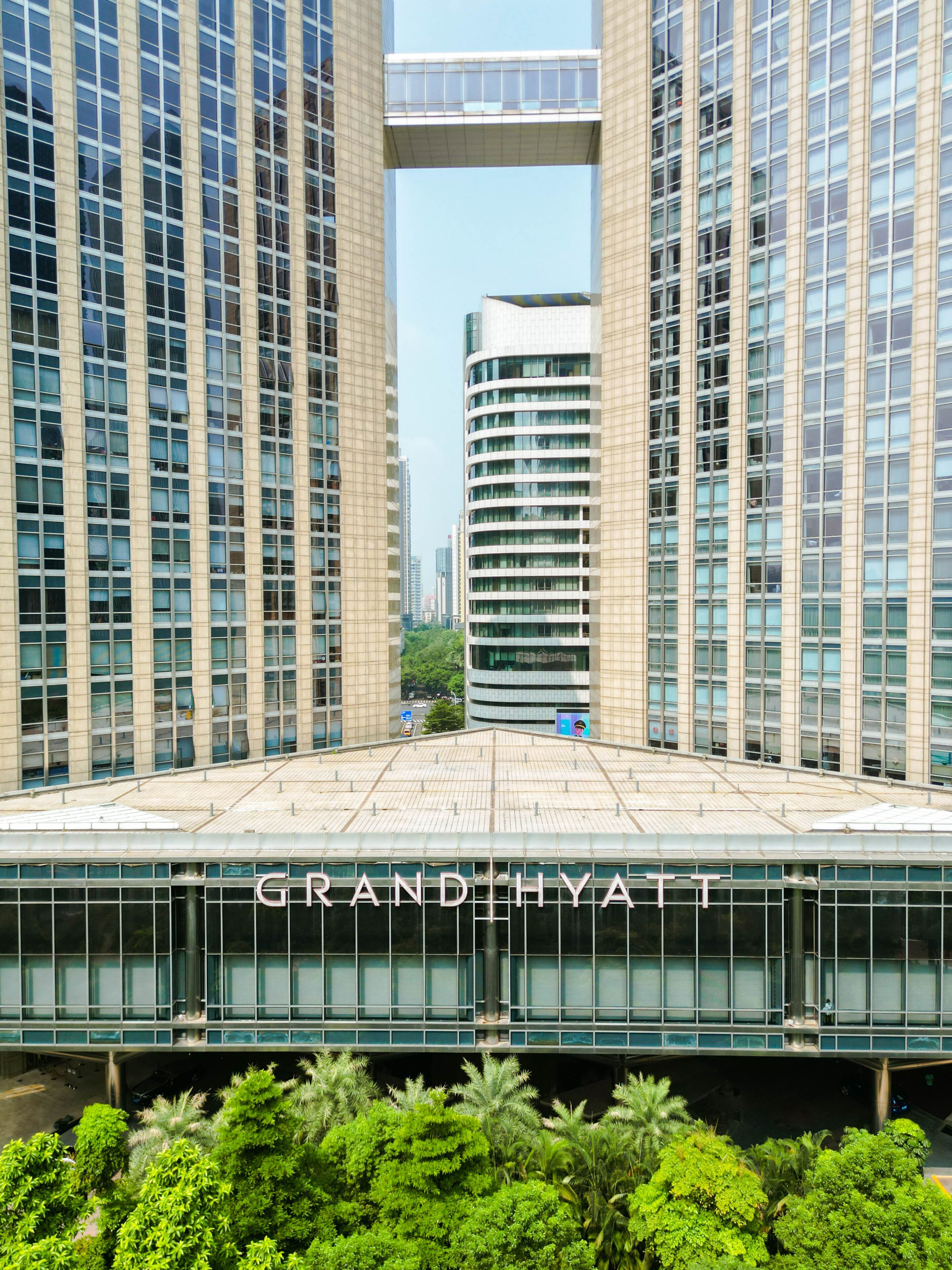 A modern hotel with a prominent glass facade, a central atrium, and lush greenery in front.