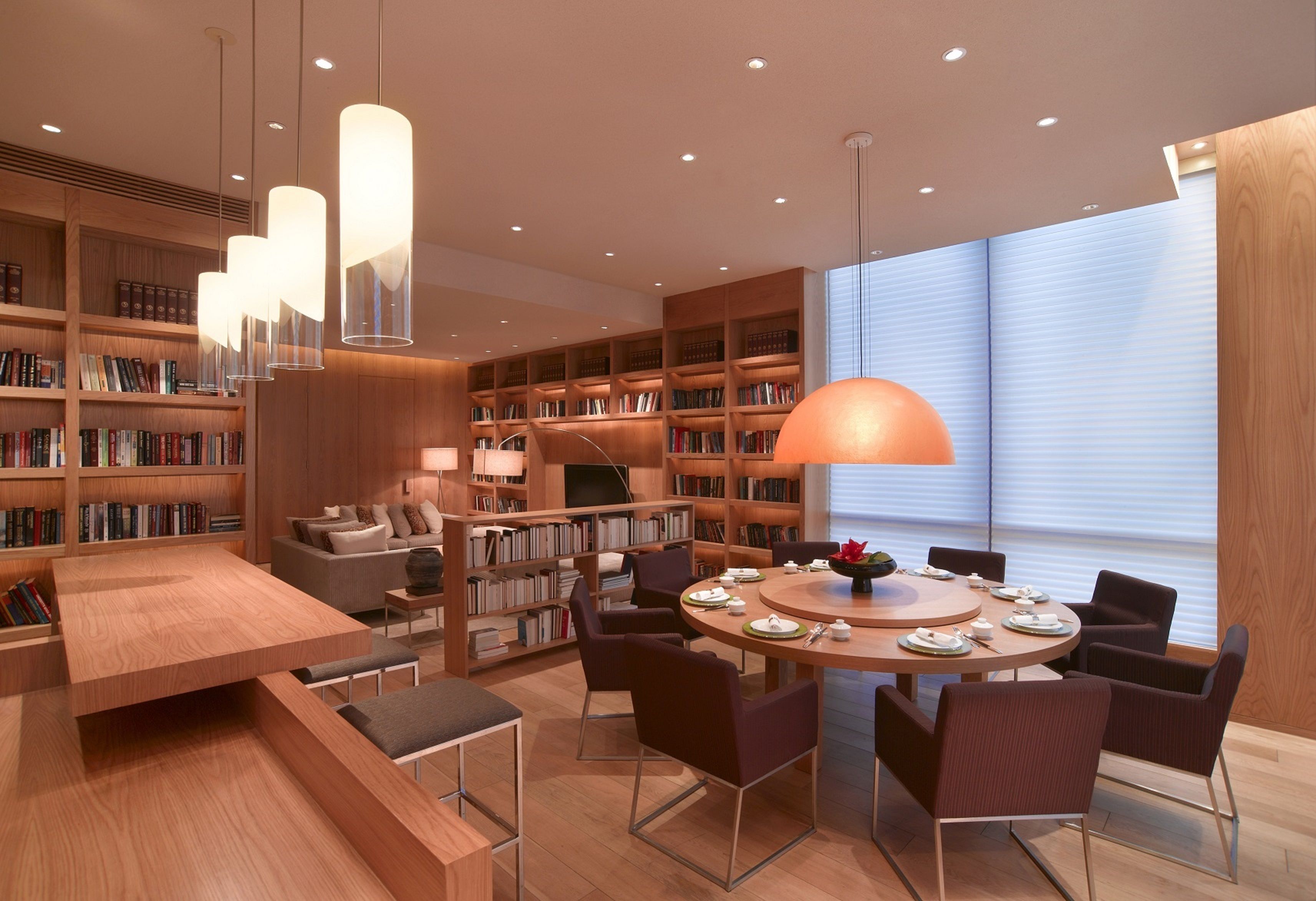A modern library with a round dining table, bookshelves, and comfortable seating.