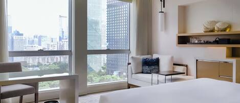 A hotel room with a bed, a seating area with a table, a desk, and a view of the cityscape through large windows.