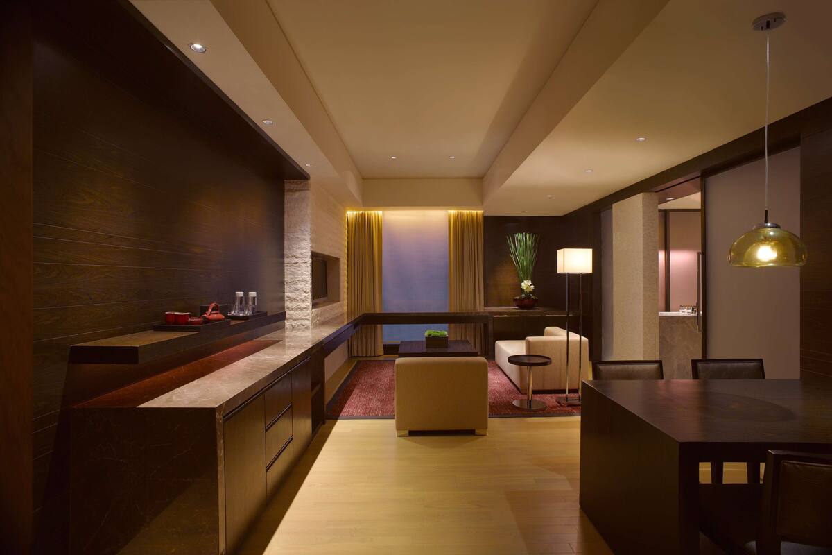 Een moderne hotelkamer met een keukenhoek, een zithoek met een bank en stoelen, en een eettafel.