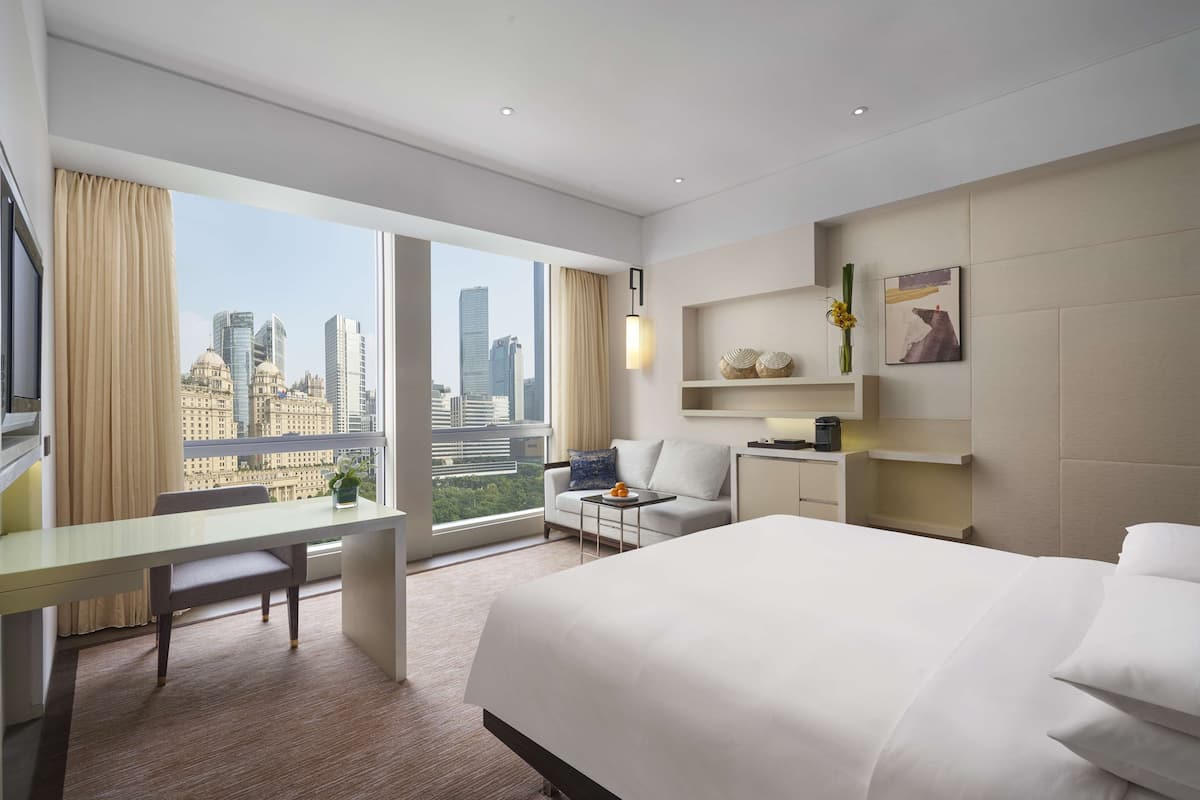 Een moderne hotelkamer met een groot bed, een bureau, een bank en uitzicht op de stad.