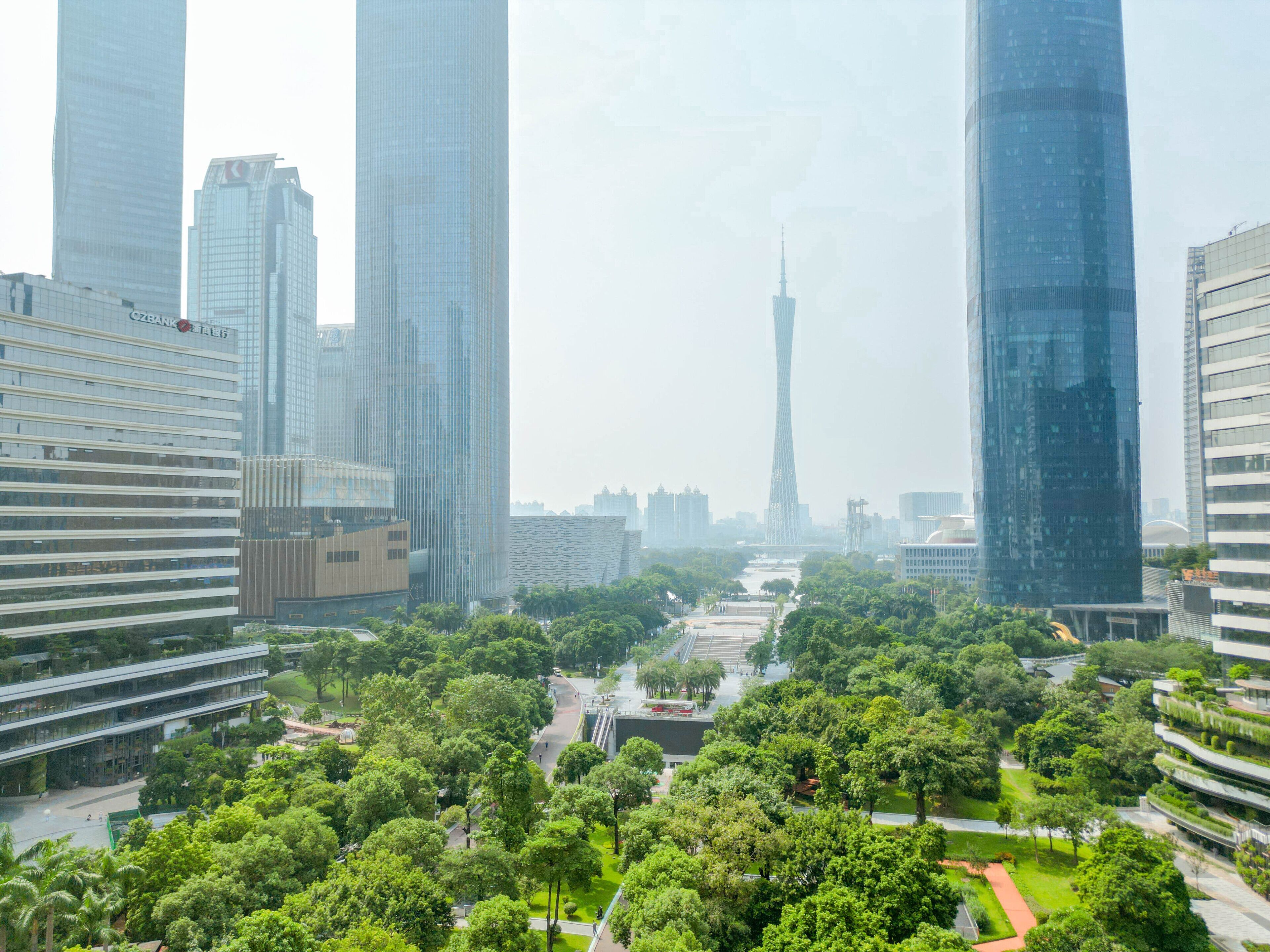 A cityscape with modern skyscrapers, a prominent tower in the distance, and a well-maintained park area with pathways.