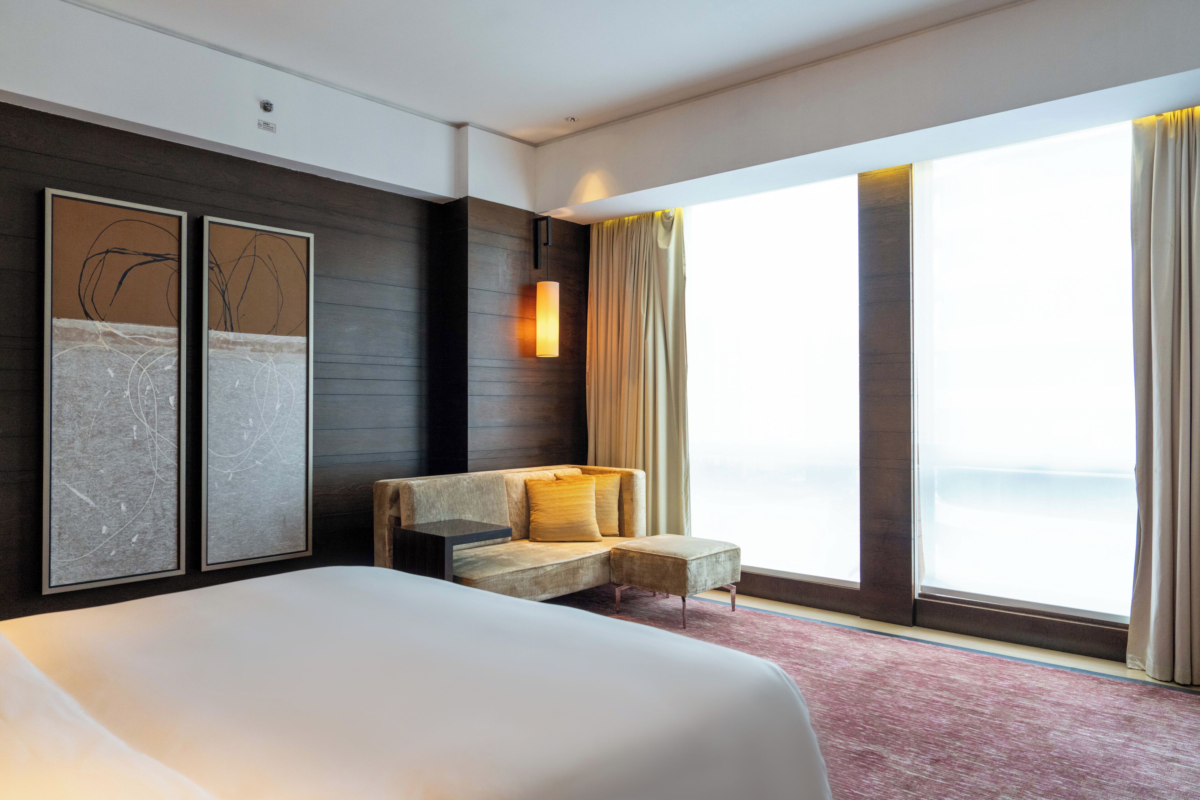 Habitación de hotel con una cama grande, un sofá, una mesita, cuadros en la pared, una ventana con cortinas y vista al mar.