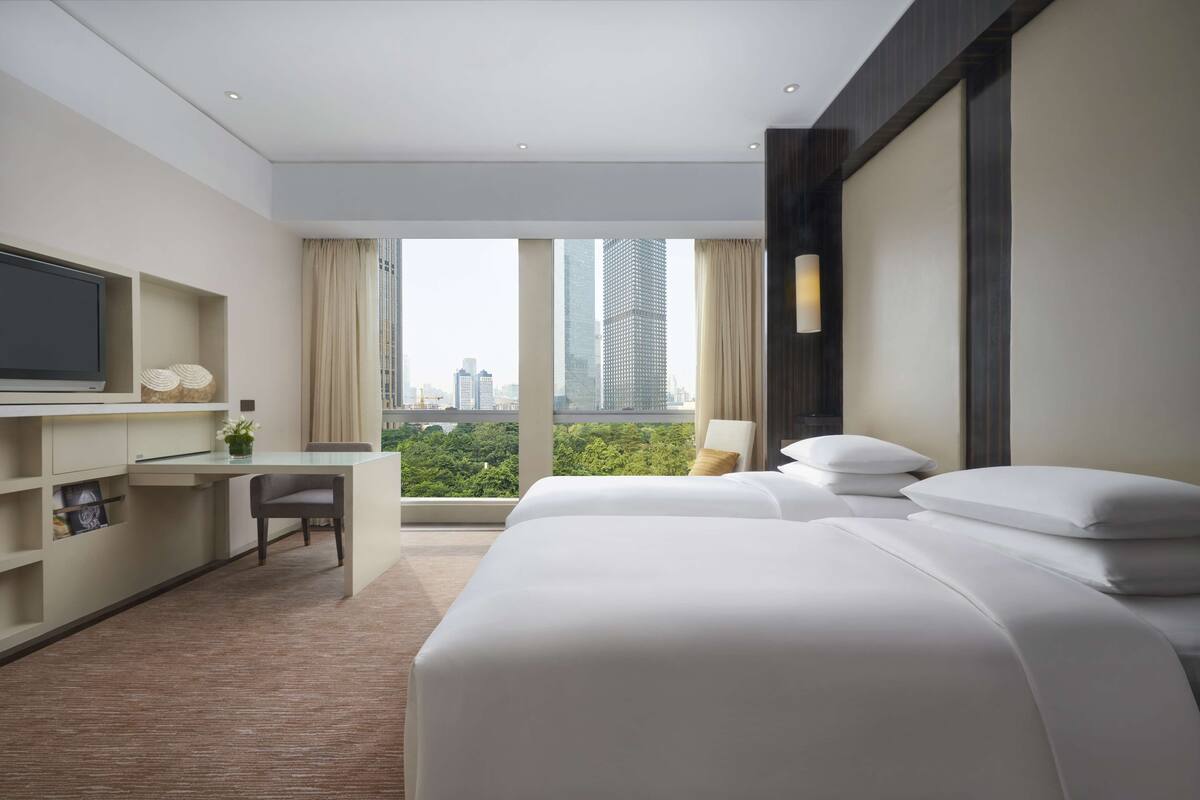 Een hotelkamer met een bed, een bureau, een stoel, een televisie en een groot raam met uitzicht over de stad.