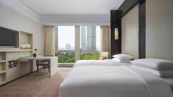 Ein Hotelzimmer mit Bett, Schreibtisch, Stuhl, Fernseher und einem großen Fenster mit Blick auf die Stadt.