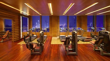 A modern gym with treadmills, weight machines, and a city view through large windows.