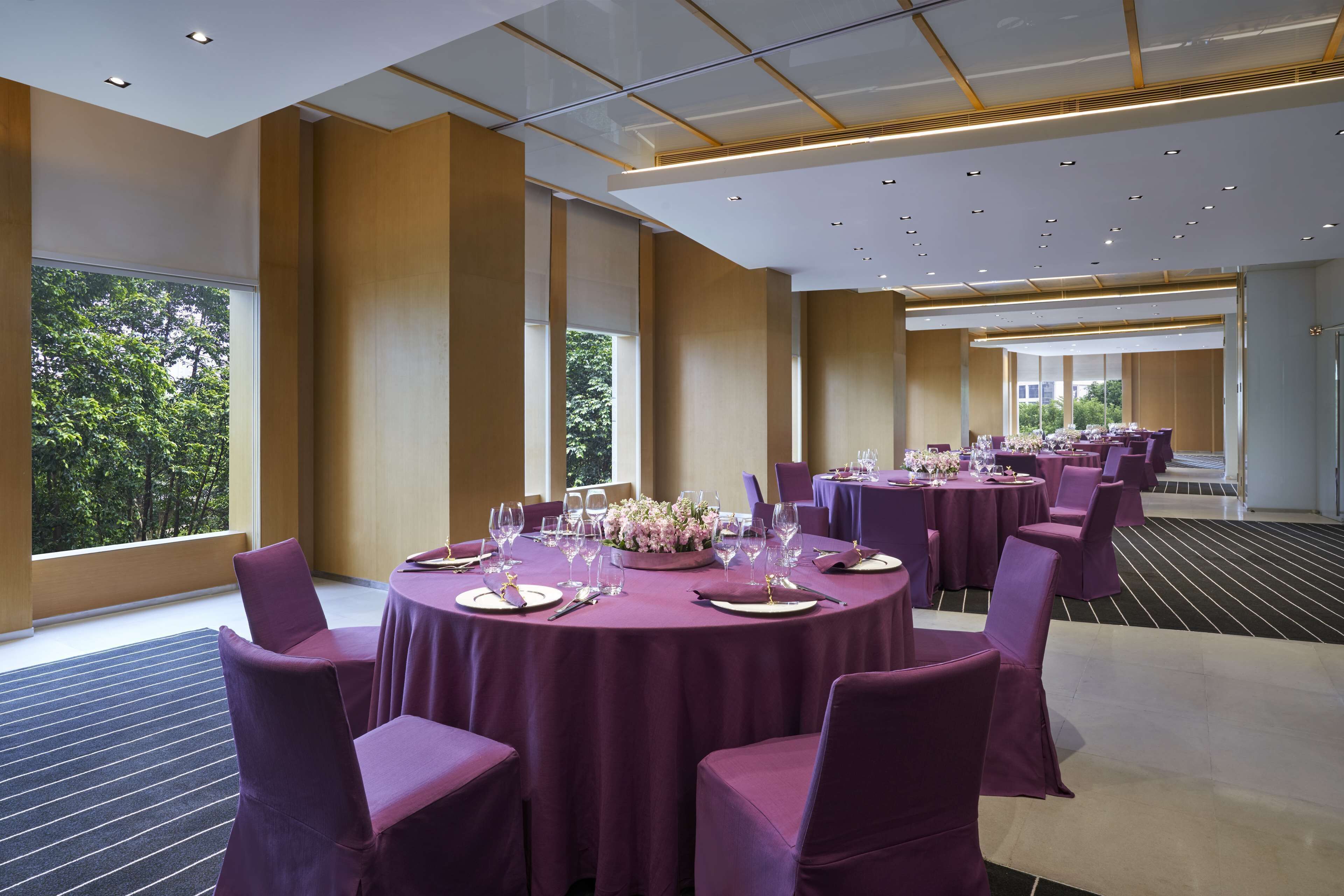 A conference room with round tables, purple chairs, and a large window with a view of trees.