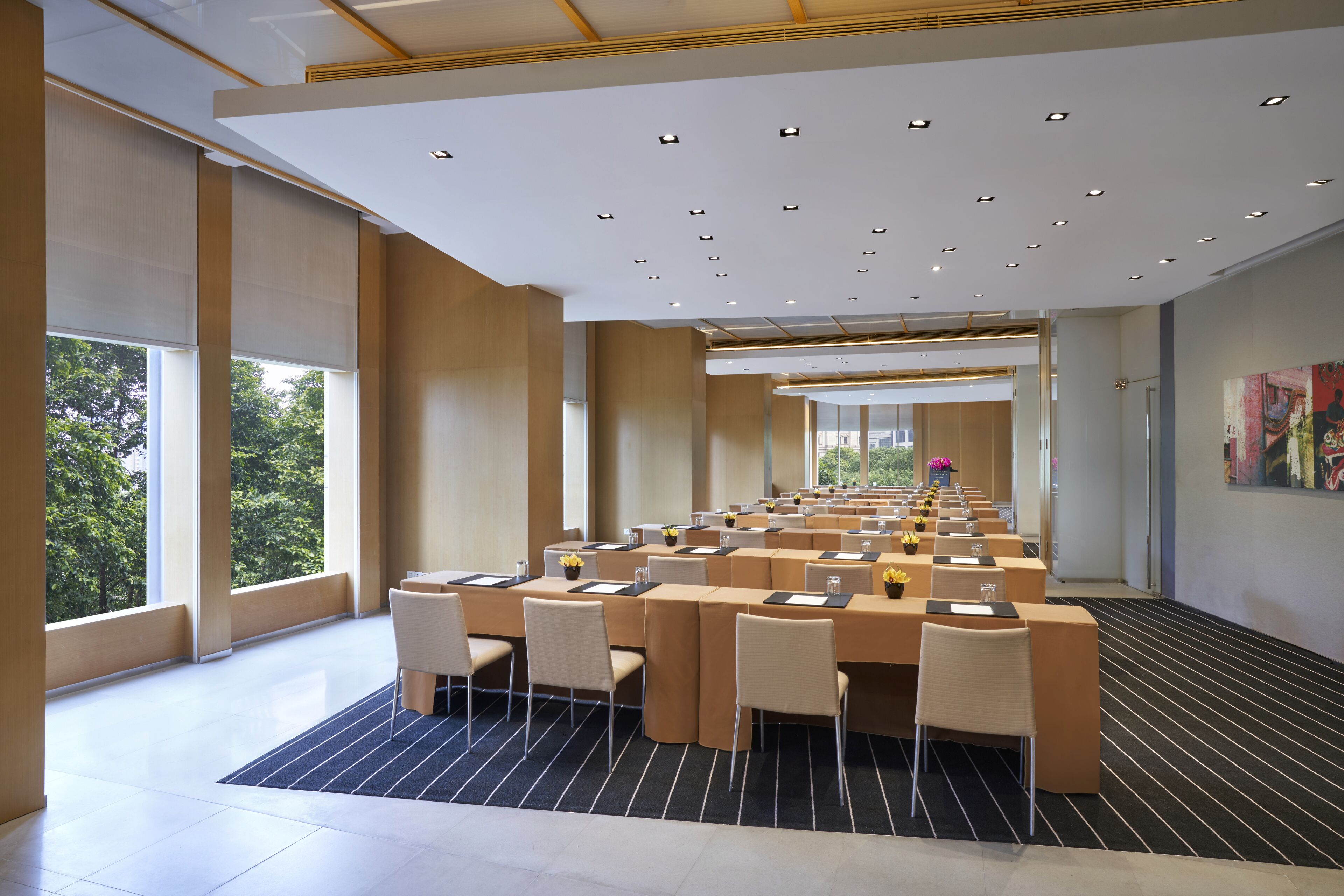 A spacious conference room with multiple tables and chairs, large windows, and a modern ceiling design.