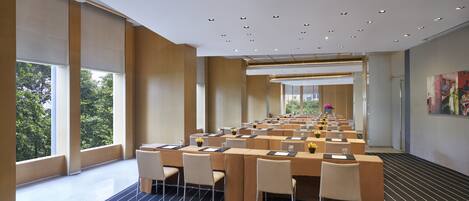 A spacious conference room with multiple tables and chairs, large windows, and a modern ceiling design.