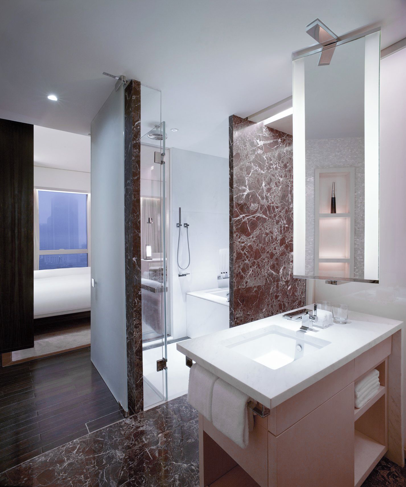 A modern bathroom with a glass shower enclosure, a marble-topped sink, and a large mirror.