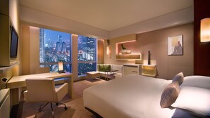 Habitación de hotel moderna con una cama grande, un escritorio y una silla. Se ve la ciudad a través de la ventana, y la habitación tiene un diseño minimalista con colores neutros.