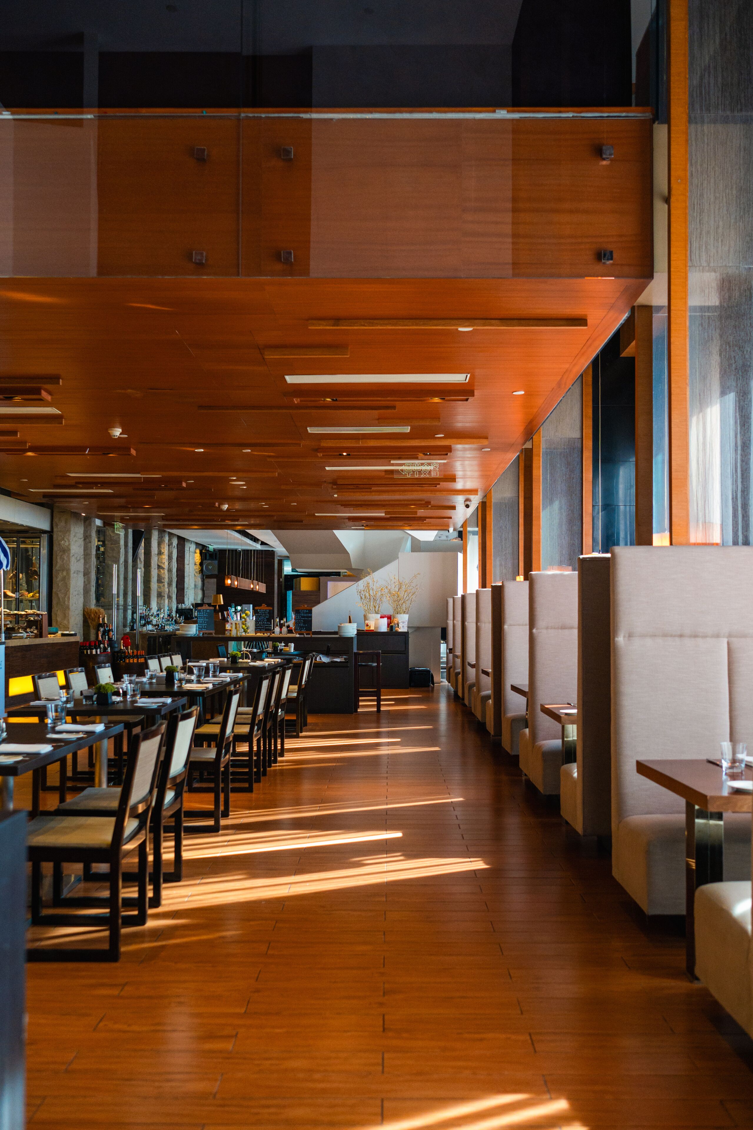 A modern restaurant interior with wooden panel ceilings, long dining tables, and booths.