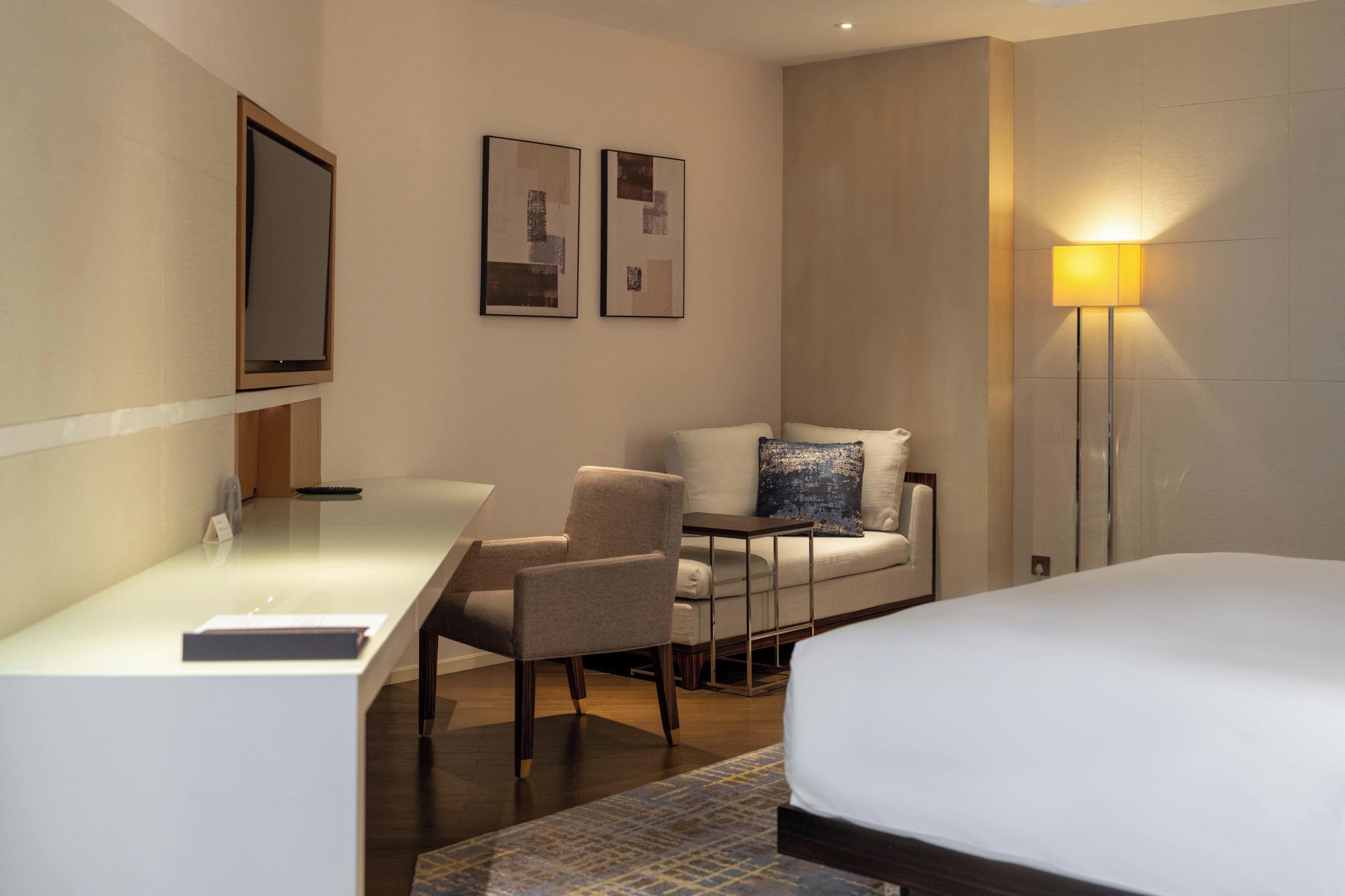 Una habitación de hotel con cama, escritorio, silla, sofá y lámpara de pie.