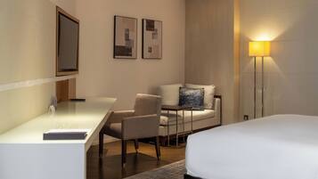 Una habitación de hotel con cama, escritorio, silla, sofá y lámpara de pie.
