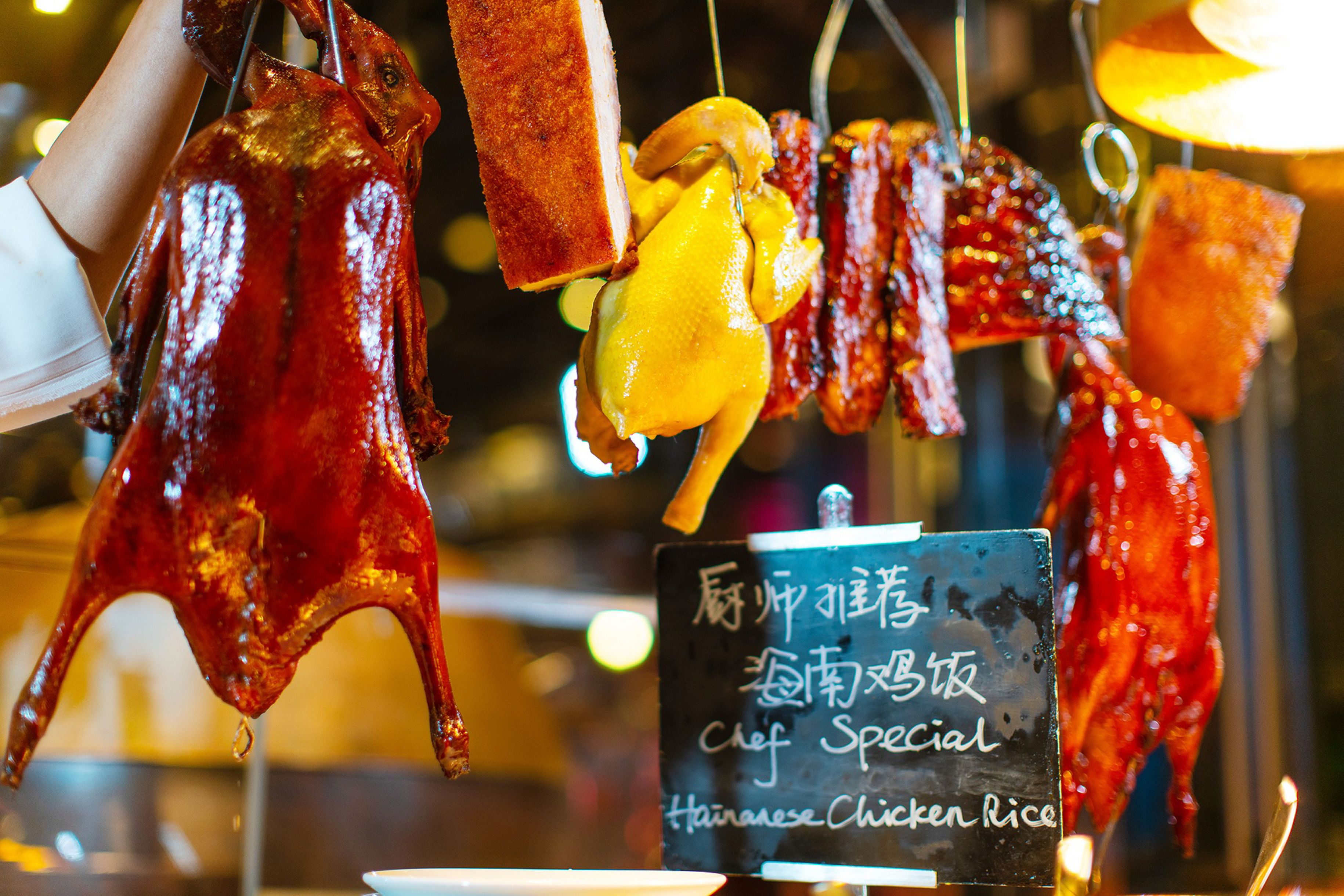 A variety of roasted meats displayed for sale, including a prominent red duck and a yellow chicken, with a sign indicating a special Chinese chicken rice dish.