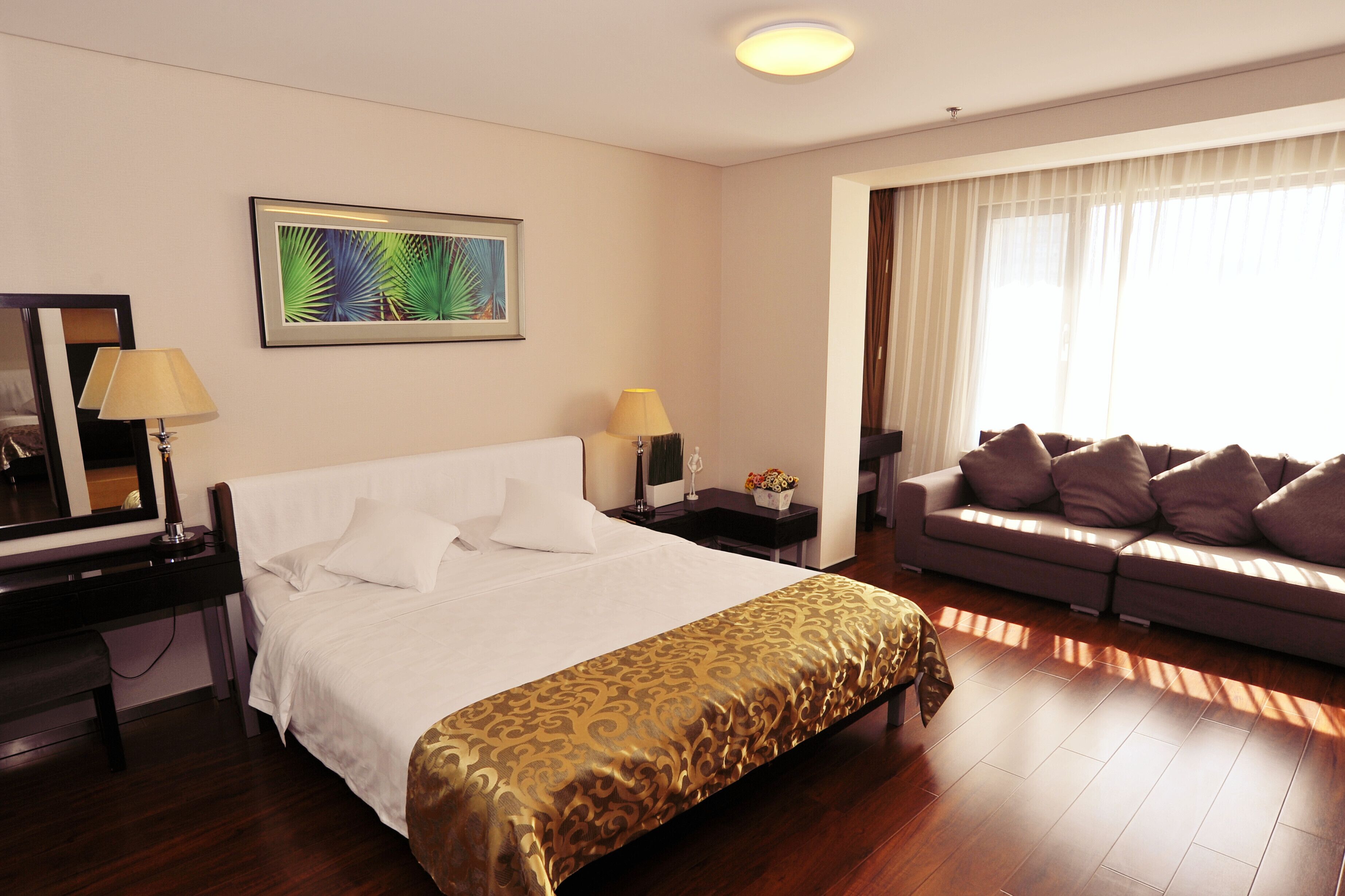 A hotel room with a bed, a desk, a chair, a sofa, a window with curtains, and a framed picture on the wall.