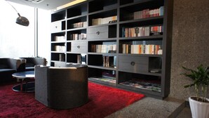 Een moderne woonkamer met een grote boekenkast, een rond poef en een rood vloerkleed.