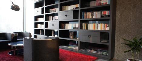Ein modernes Wohnzimmer mit einer großen Bücherwand, einem runden Ottomanen und einem roten Teppich.