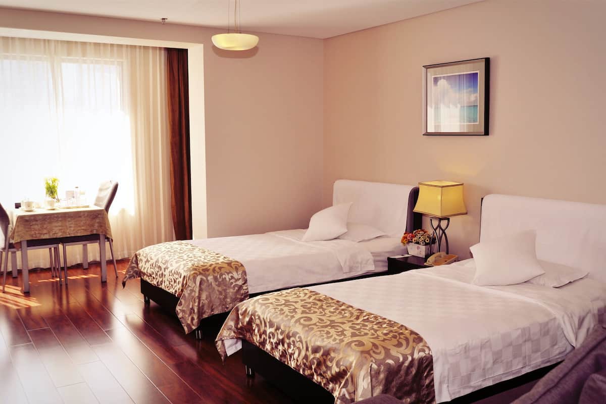 Una camera d'albergo con due letti, una scrivania con una sedia, una lampada e un quadro appeso al muro.