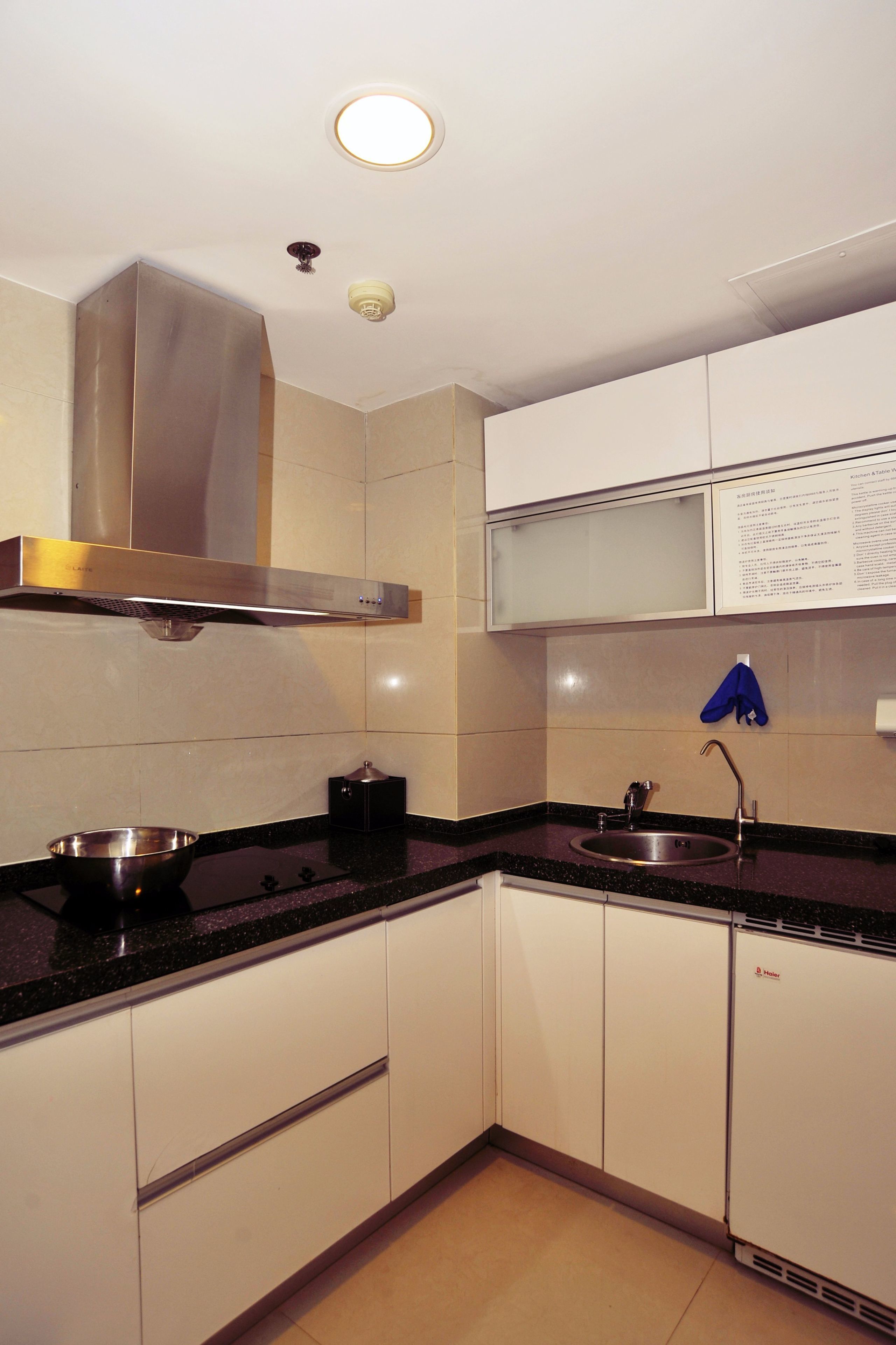 A modern kitchen with white cabinets, a stainless steel range hood, a black countertop, and a sink.