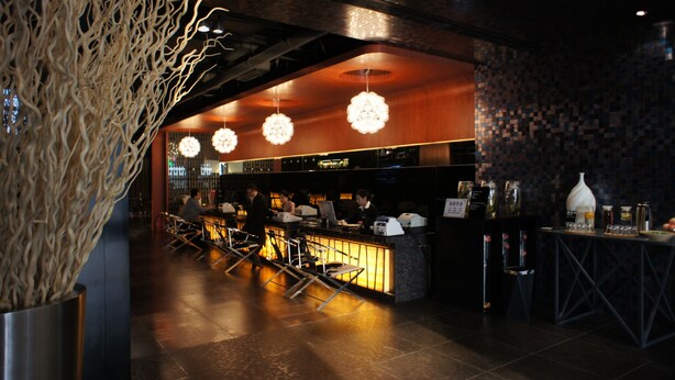 Een bar met een toonbank, barstoelen en hangende sferische lampen.