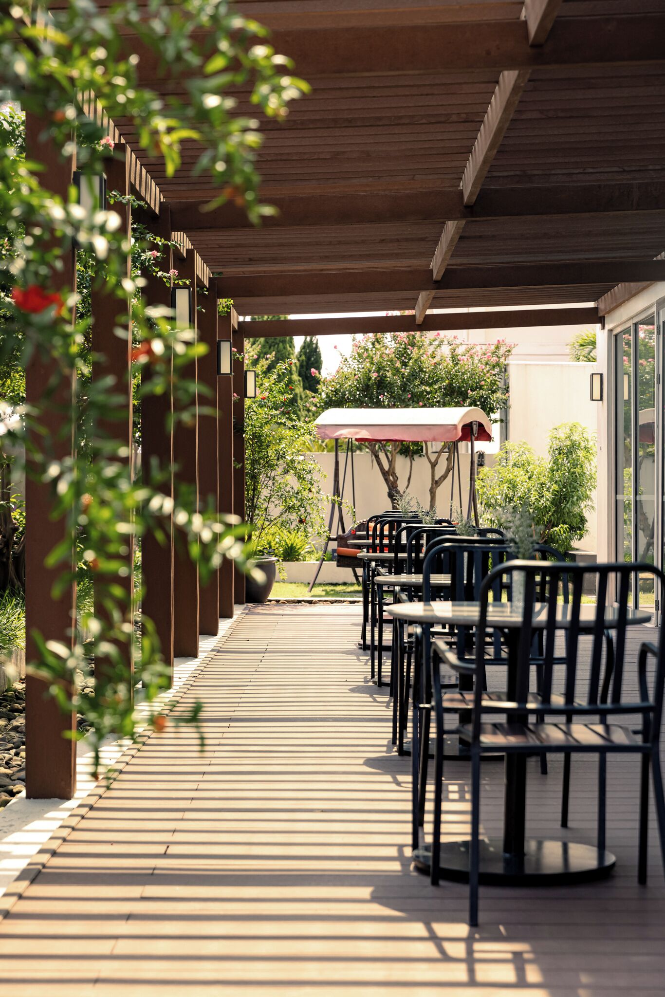 A covered outdoor seating area with tables and chairs, a wooden ceiling, and potted plants.