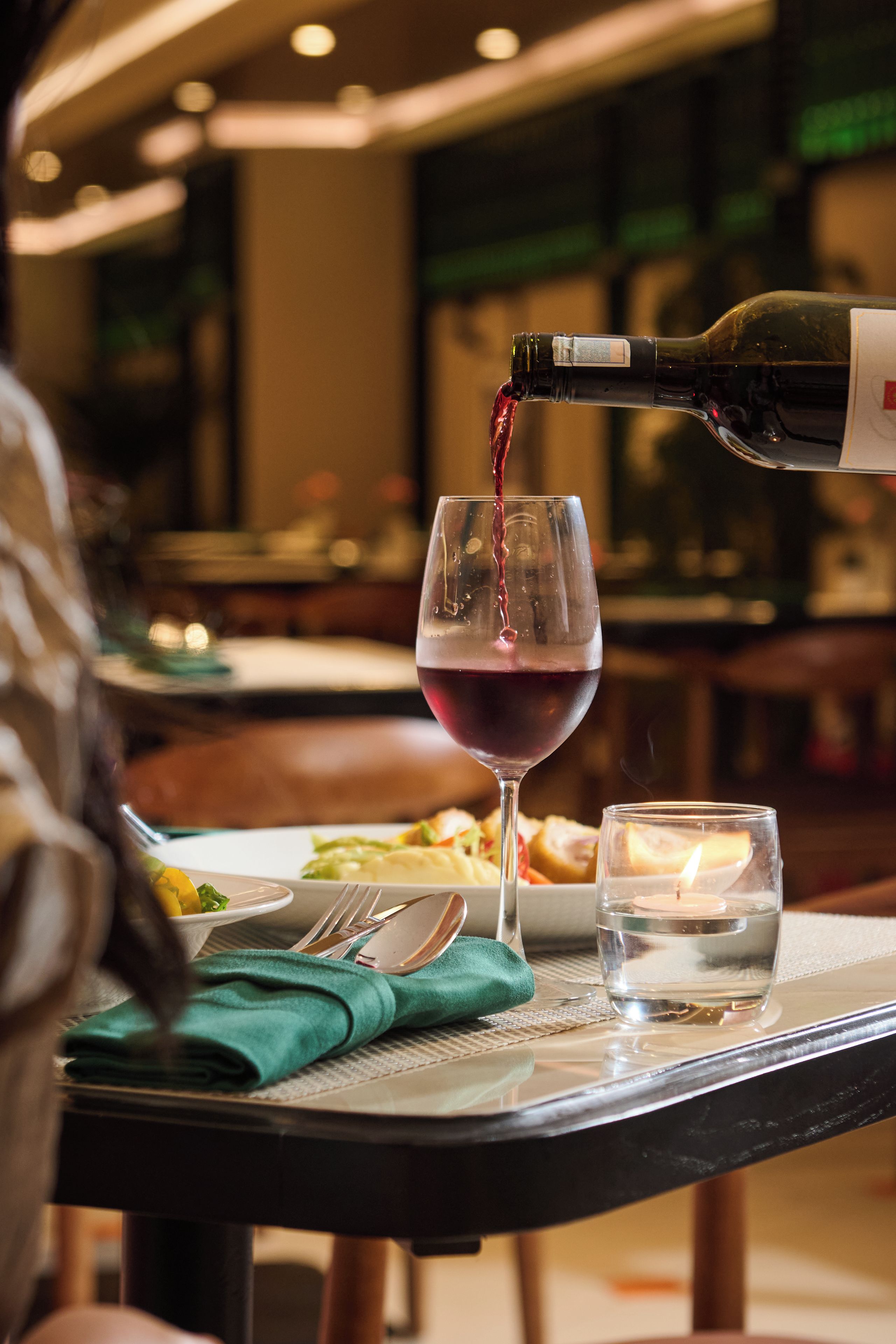 Una mesa de comedor con una copa de vino, una botella de vino tinto y un vaso de agua.