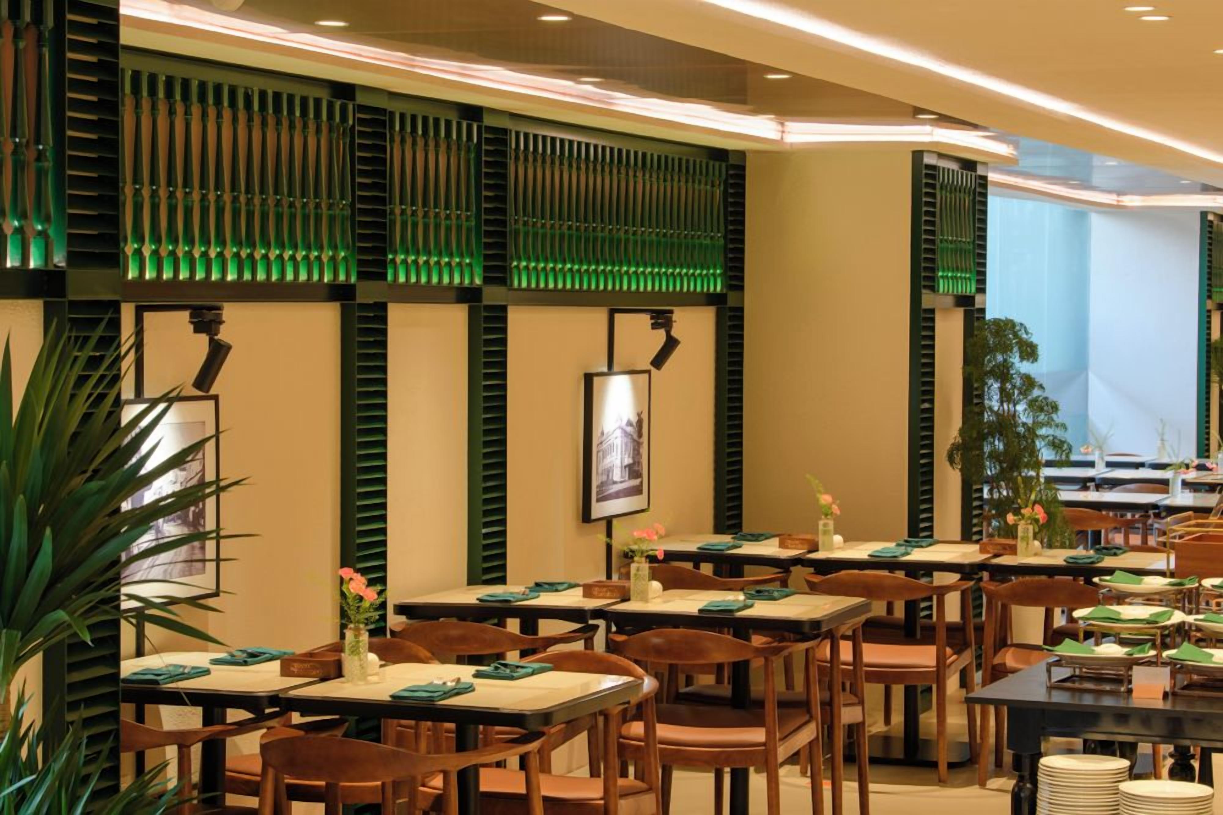 A restaurant interior with multiple tables and chairs, green decorative panels, and a framed picture on the wall.